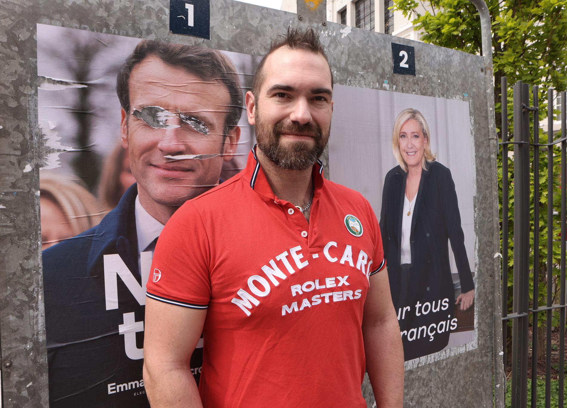 Le Pen-väljaren Amori Fontaine framför valafficher av kandidaterna.