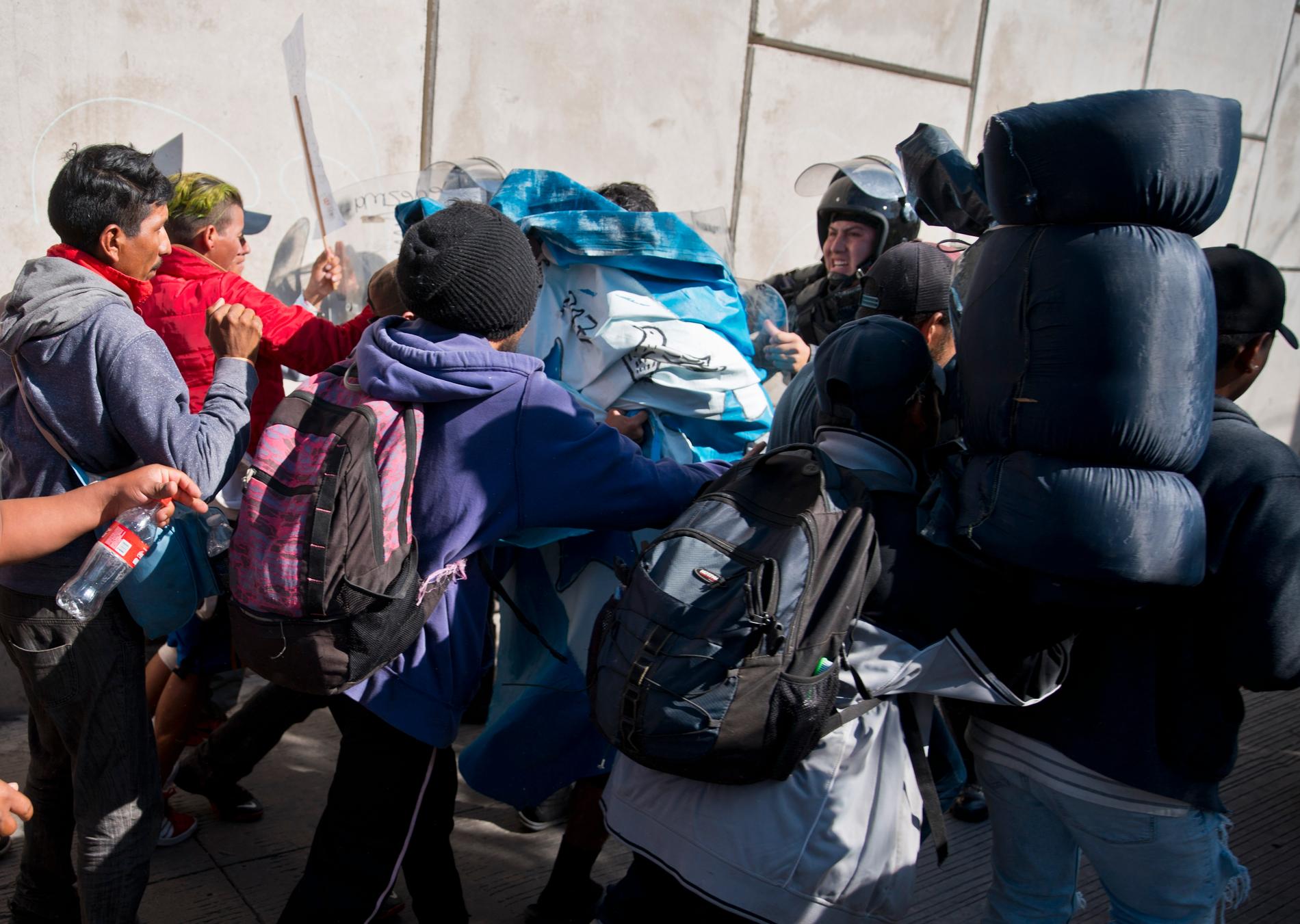 Migranter pressar på mot polisen vid gränsövergången i Tijuana i Mexiko.