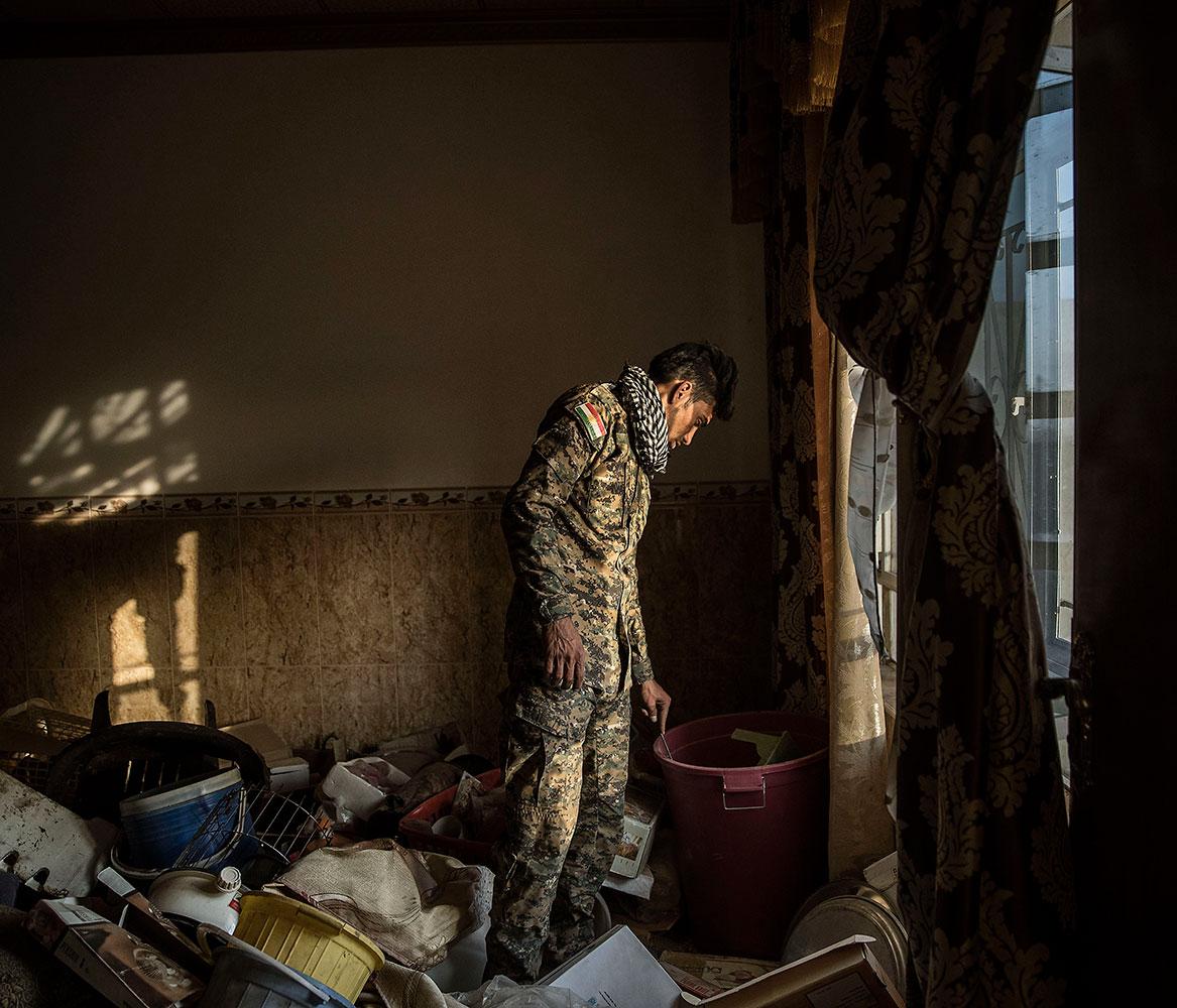 En kurdisk soldat går igenom sakerna i ett hus som nyss återtagits från IS.