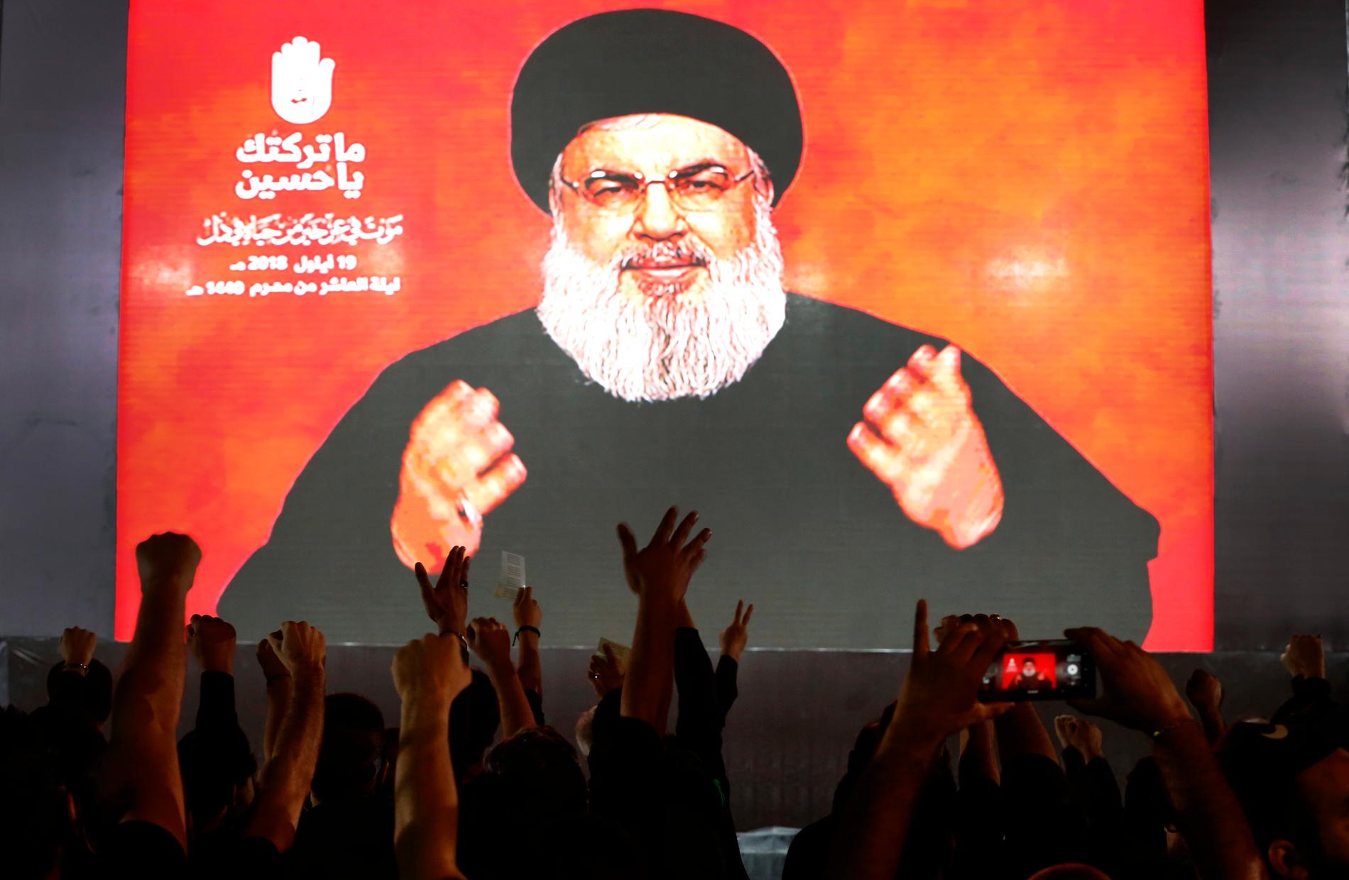 Hizbollahs ledare Hassan Nasrallah talar via videolänk, medan anhängare till honom lyfter händerna i luften under ett möte i Beirut på onsdagen.