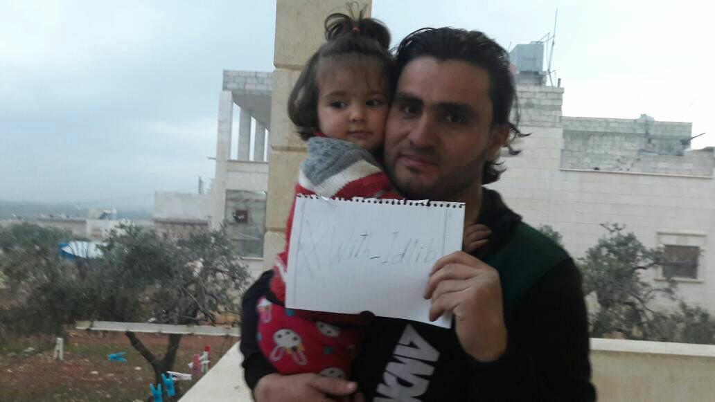 Den syriske läraren och aktivisten Abdulkafi Alhamdo tillsammans med dottern Lamar, i staden Atarib mellan Aleppo och Idlib, i januari 2018. I handen håller han en lapp som uppmanar till solidaritet med oppositionsfästet Idlib, där det pågår en omfattande regeringsoffensiv.