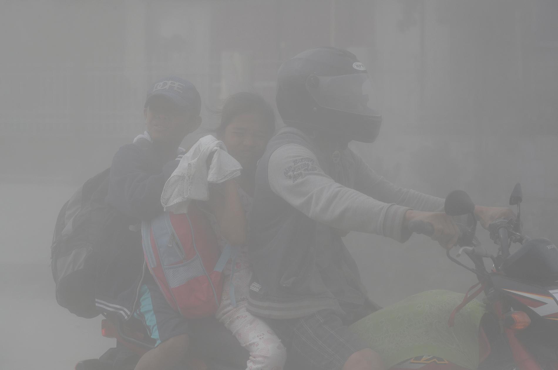 En familj åker moped genom den fallande askan under evakueringen i Cavite-provinsen. 