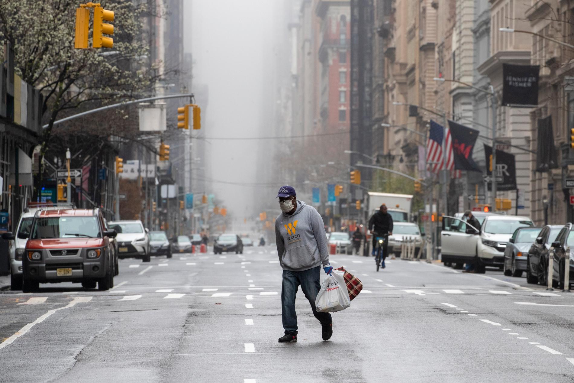 En man med munskydd korsar femte avenyn i New York.
