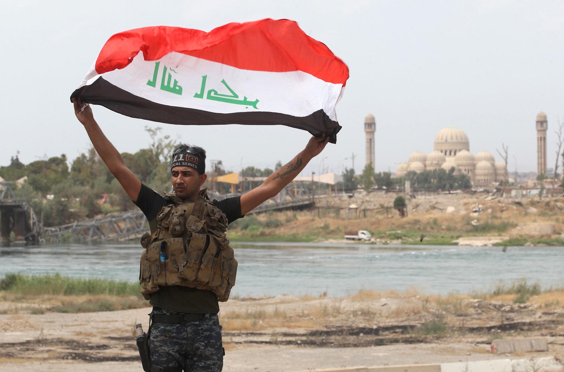 Irakisk federal polis höjer en flagga i Gamla stan i Mosul.
