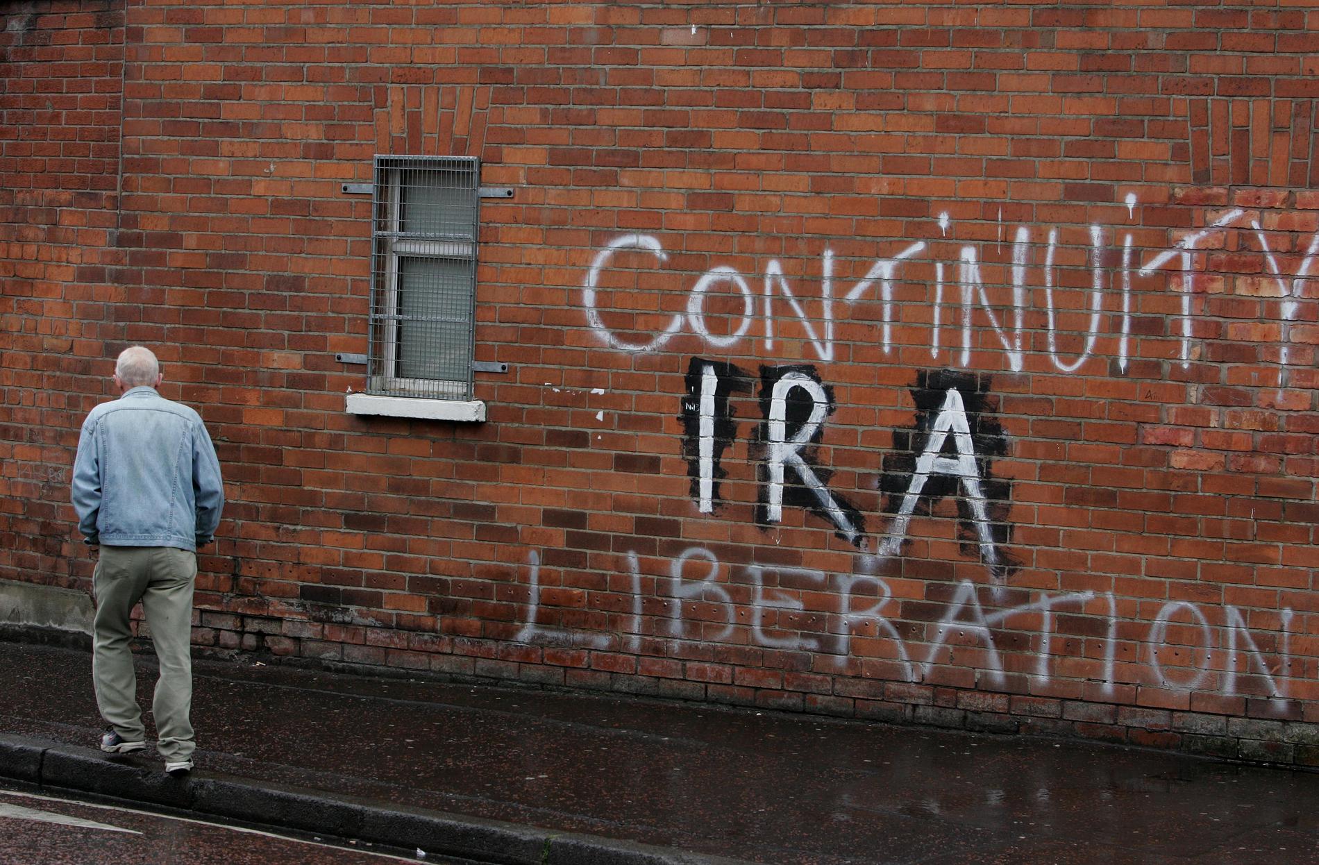 En man går förbi gammal IRA-graffiti vid Falls Road i Belfast, Nordirland.