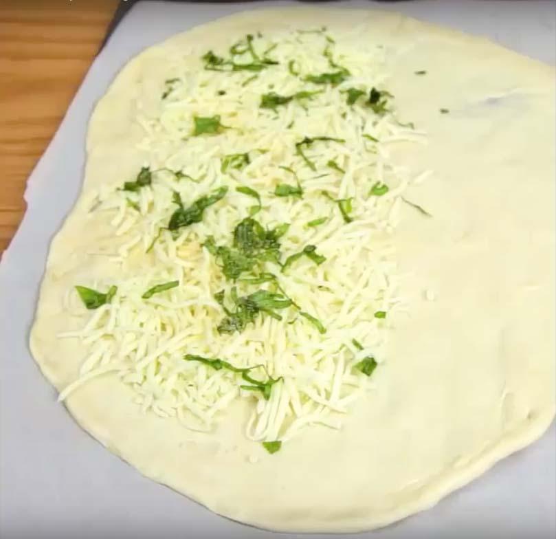 Kavla ut pizzadegen. Fördela riven ost, mozzarella, vitlökspulver och basilika på ena halvan.