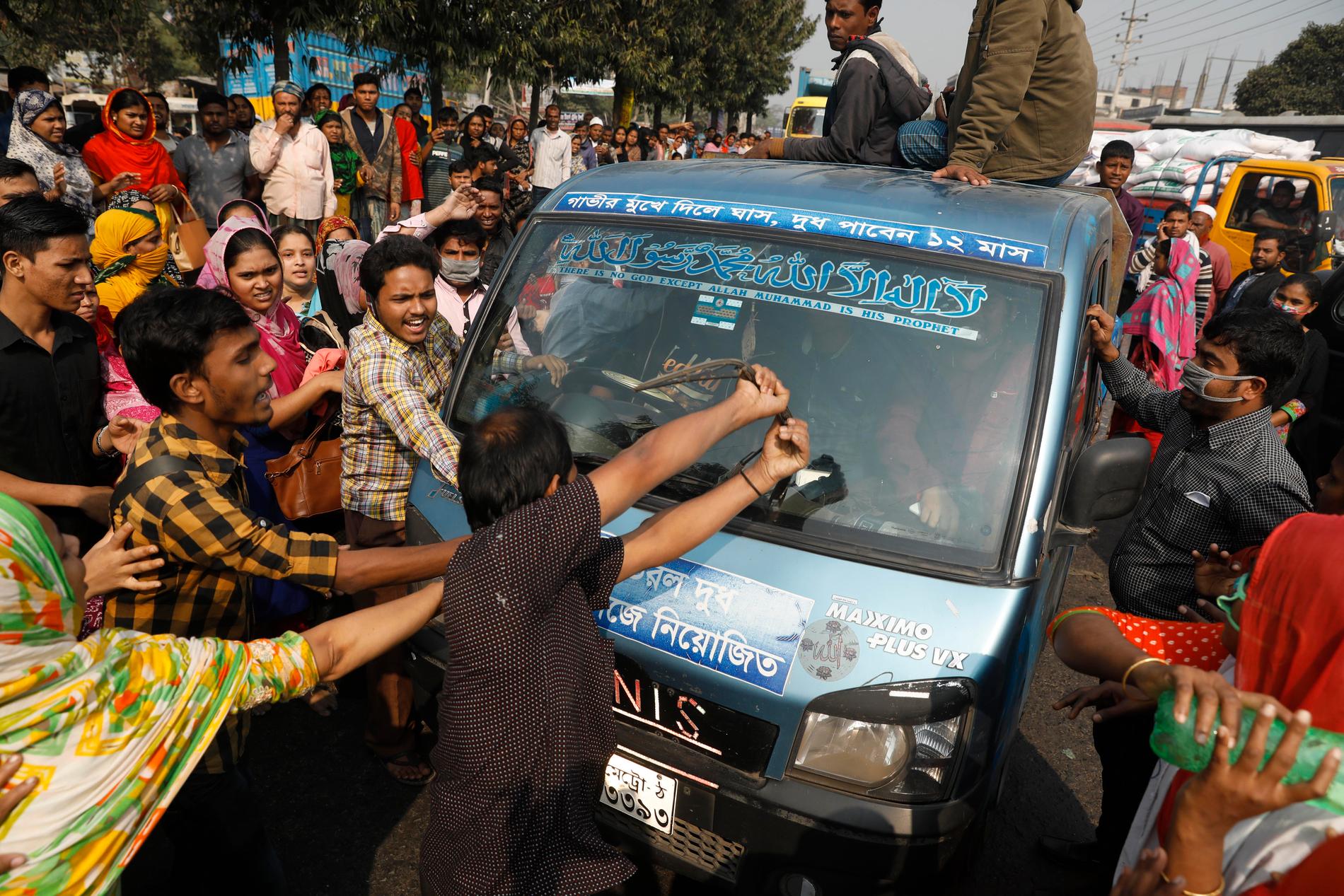 Protesterande textilarbetare i Bangladesh vandaliserar en bil i förorten Savar i Dhaka.