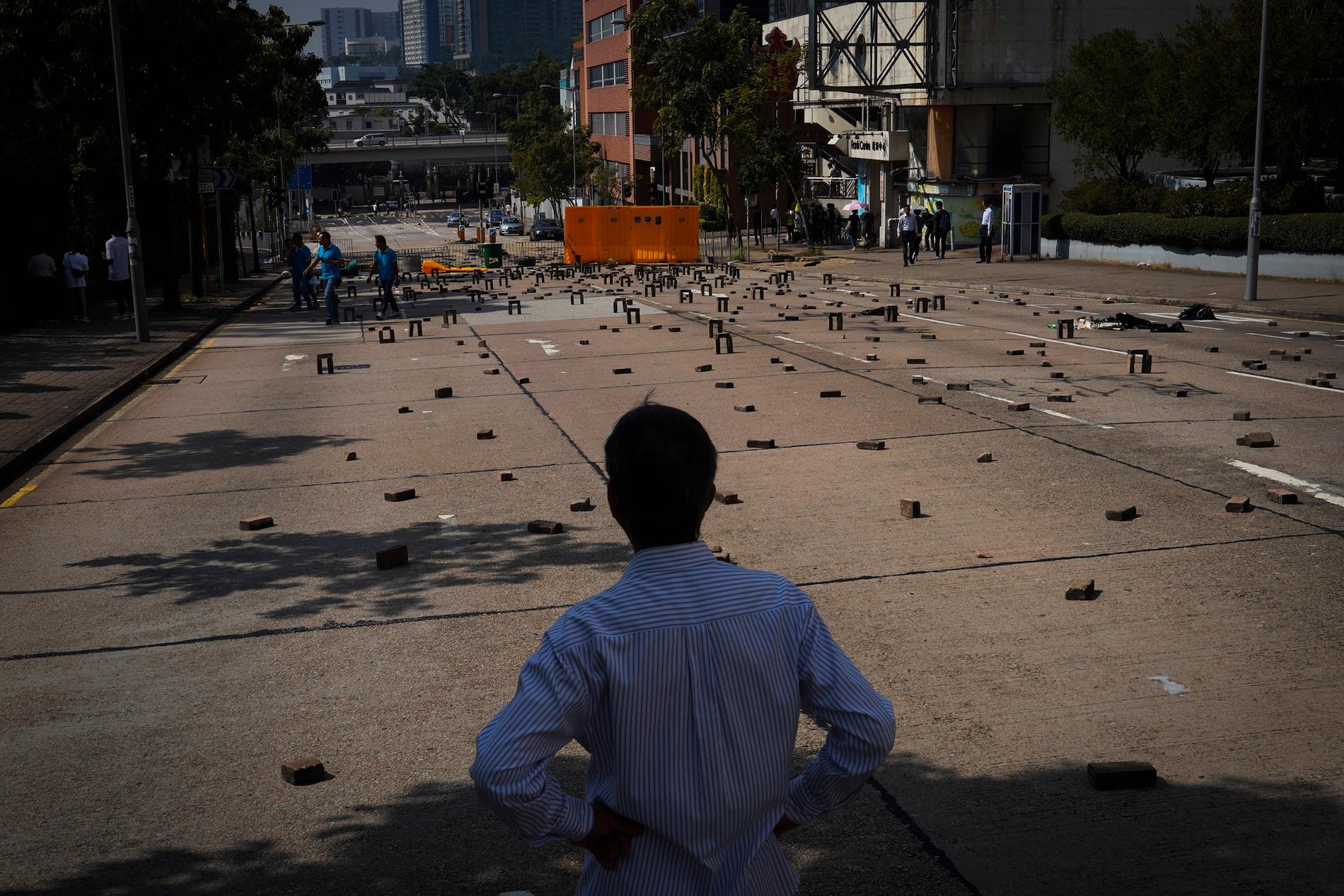 En man betraktar en väg utanför Baptist University i Hongkong där demonstranter lagt tegelstenar och satt upp barrikader under onsdagen.