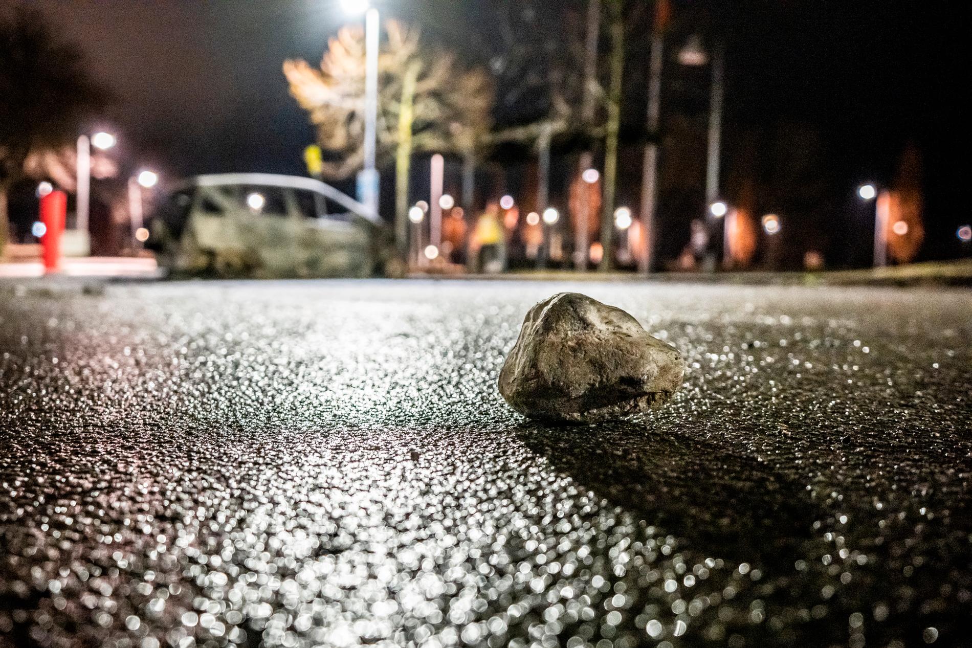 En sten syns på marken intill en utbränd bil efter upploppen. Flera maskerade personer kastade sten mot polisen tidigare under dagen.