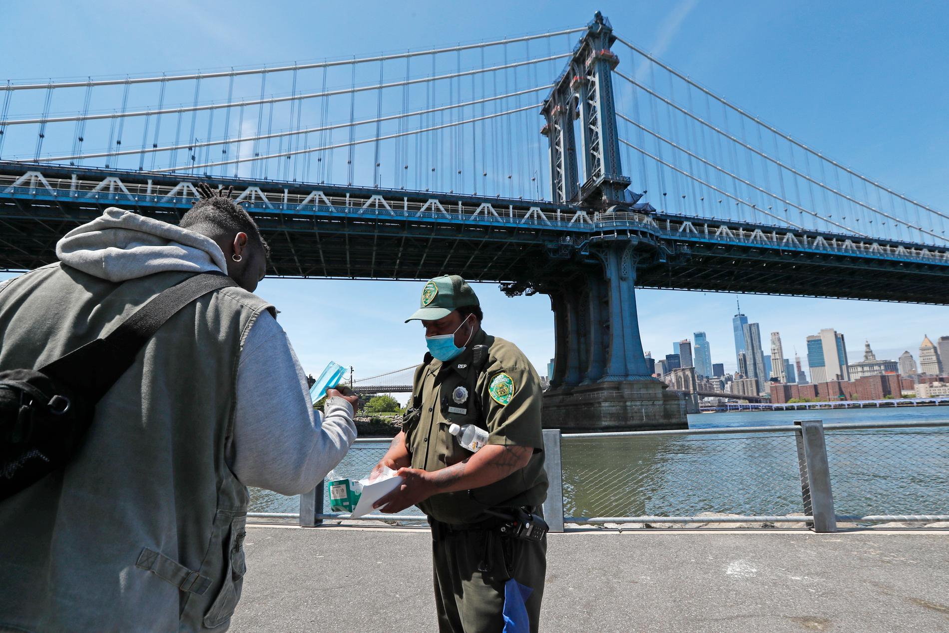 En parkvakt delar ut munskydd vid parkområdet under Brooklyn Bridge i New York.