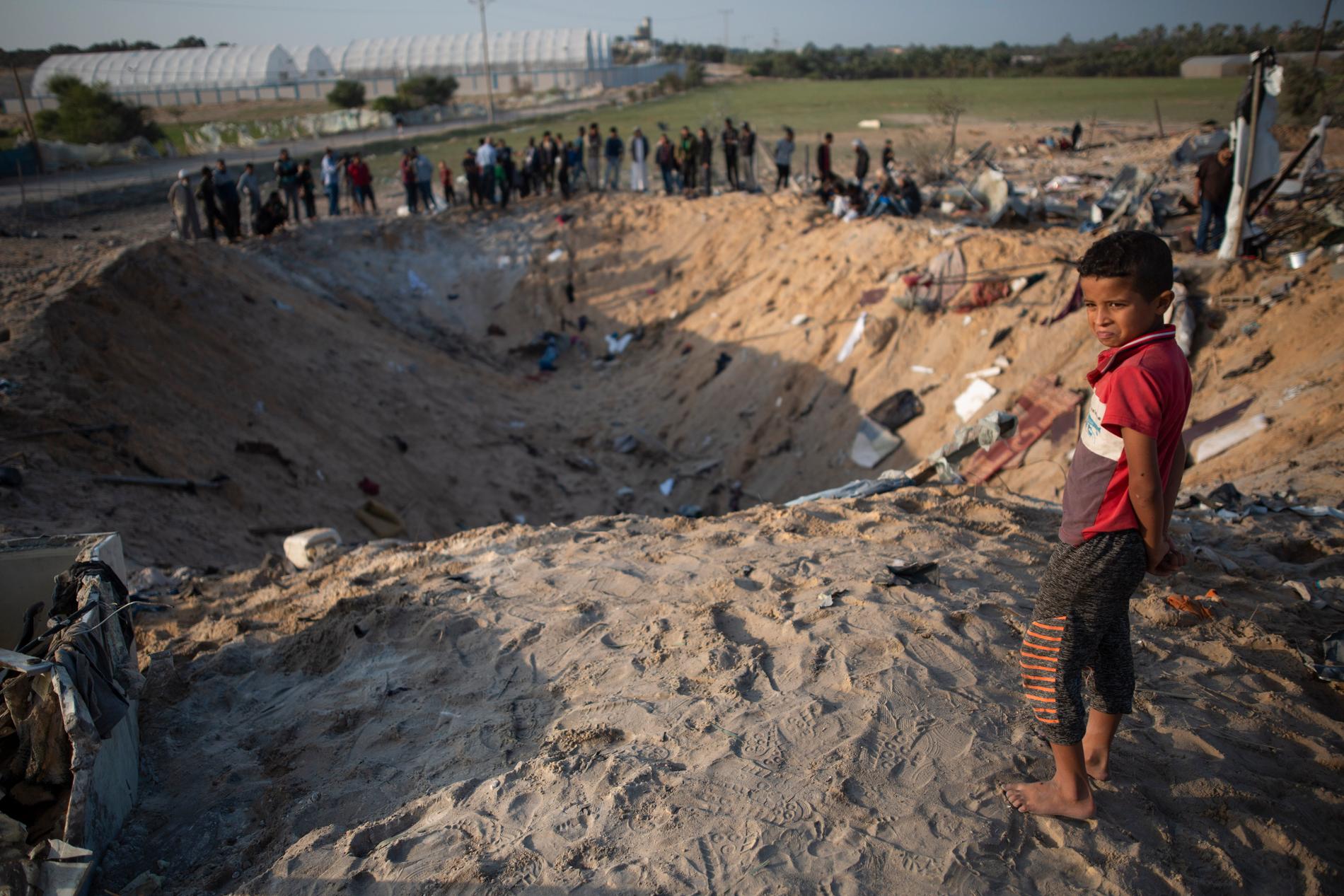 Människor som på torsdagen samlats kring kratern på Gazaremsan där Rasmi Abu Malhous bostad fanns innan den utsattes för en israelisk attack.