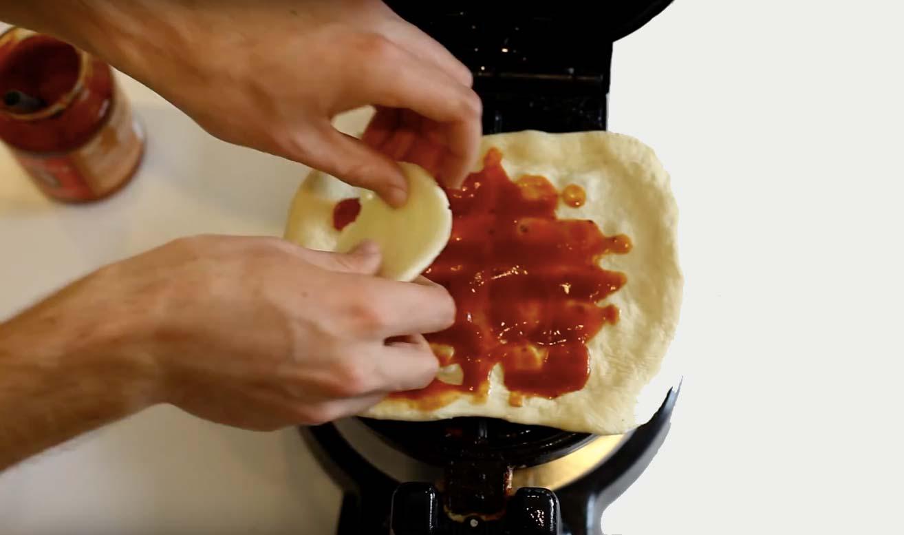 Kavla ut två mindre bottnar av pizzadegen och lägg den ena i järnet. Fördela ut tomatsåsen, men spara lite till senare.