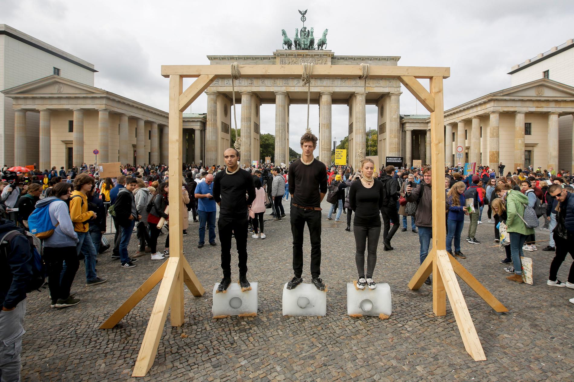 Tre personer i Berlin står på isblock under galgar med hängsnaror runt sina halsar som en protest mot den förda klimatpolitiken.