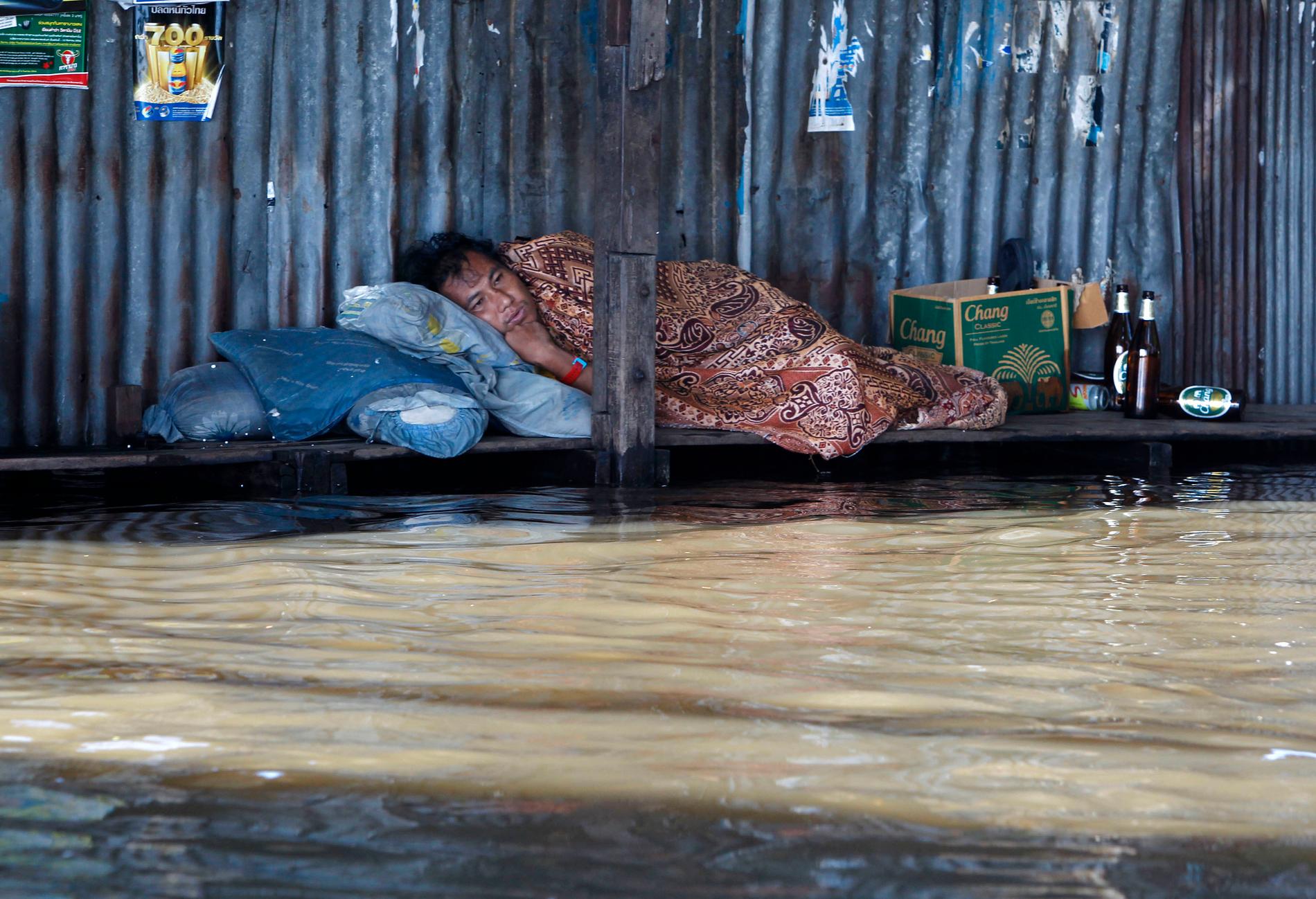 En man vilar i en tillfällig säng på en översvämmad gata i Thailands huvudstad.