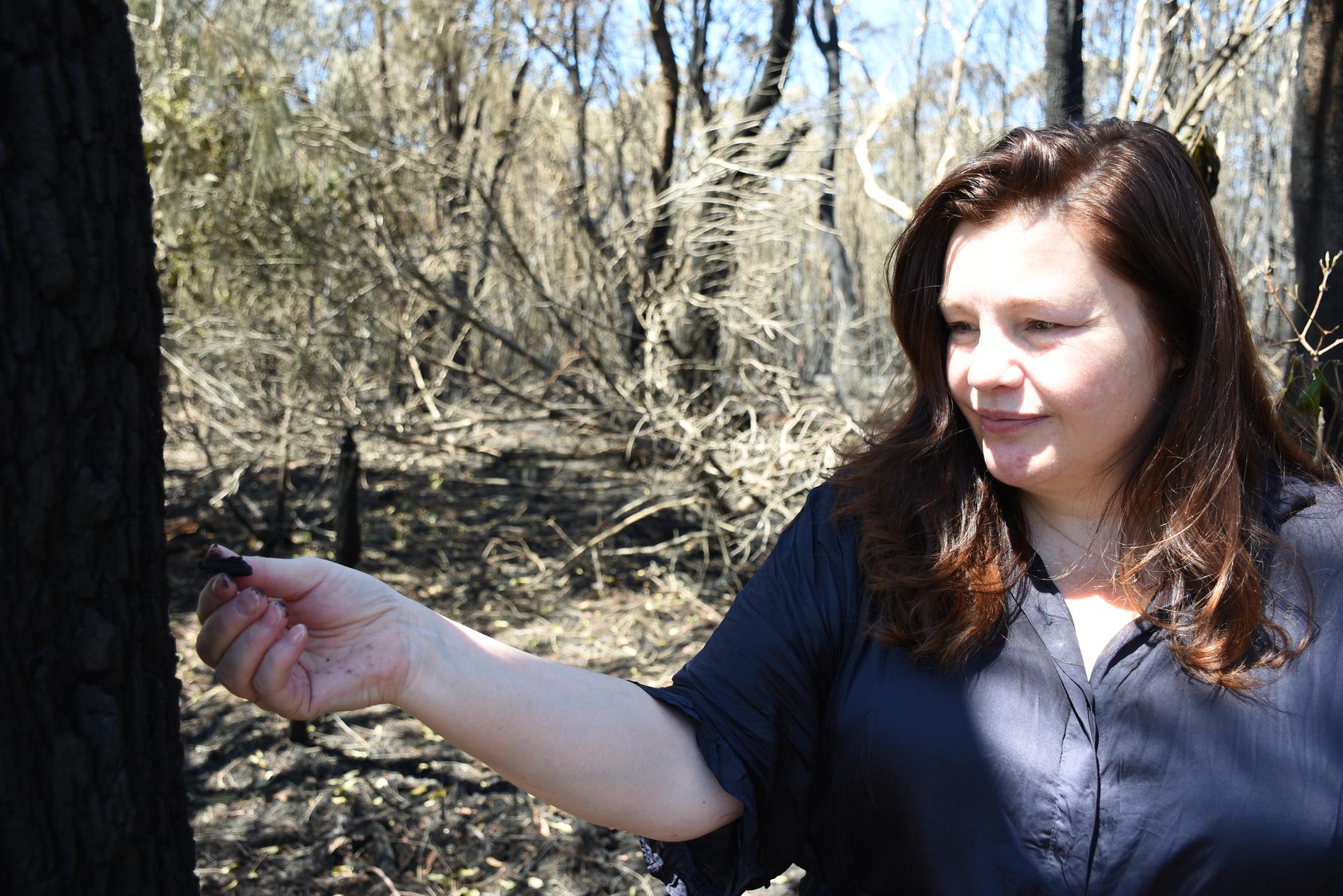 Melinda Best tar bort en bit förkolnad bark från ett träd som brann. Lågorna var mindre än 100 meter från bostäderna innan brandmännen lyckades hejda dem.