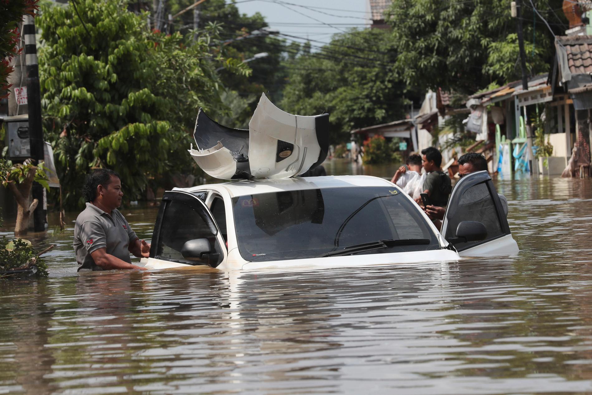 En boende i ett översvämmat kvarter i Tanggerang, utanför Jakarta, inspekterar en översvämmad bil.