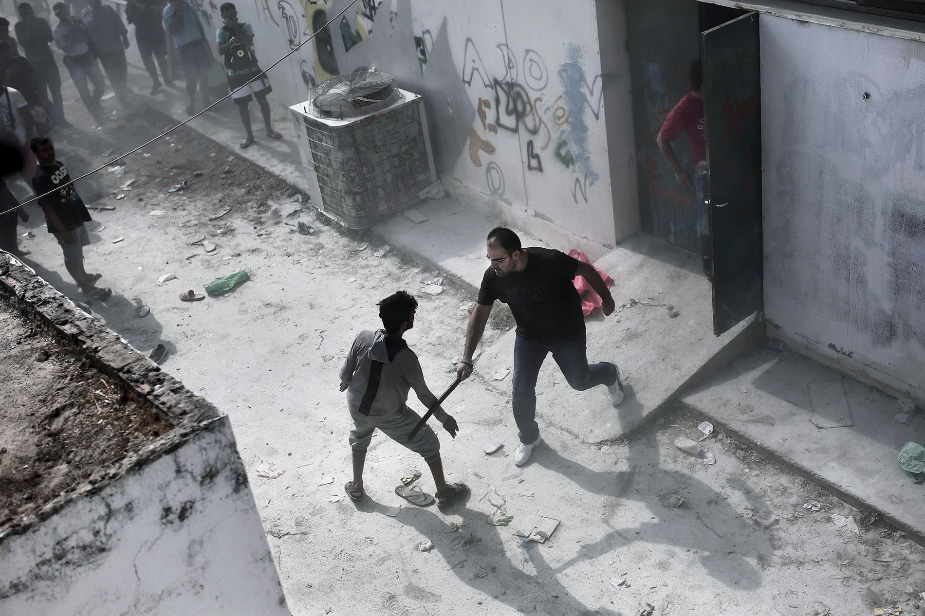 En civilklädd polisman slår mot en flykting med en batong i samband med registreringen av nyanlända på fotbollsstadium på Kos, Grekland.
