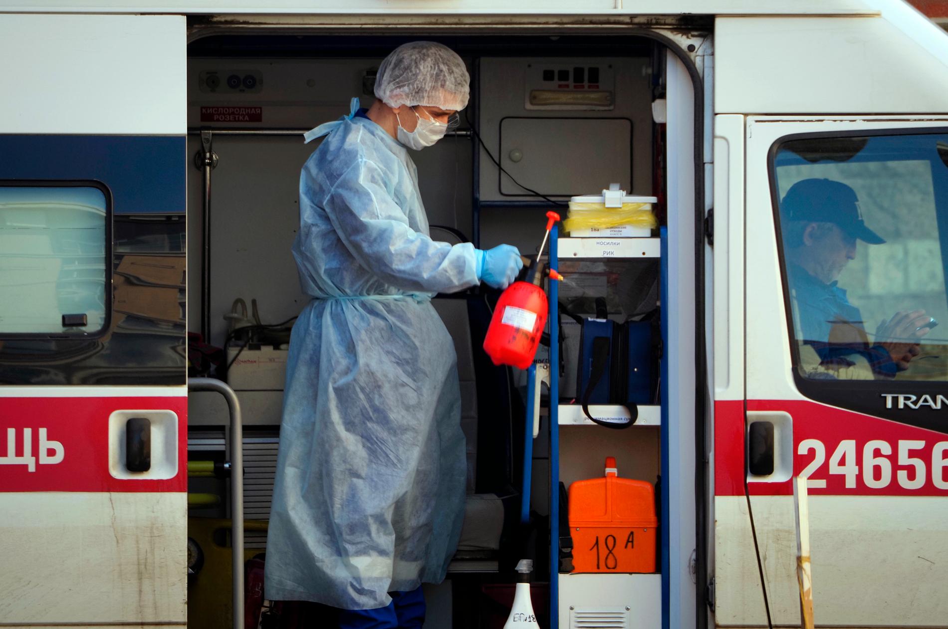 Sjukvårdspersonal i skyddsutrustning sprejar desinfektionsmedel i en ambulans i S:t Petersburg.