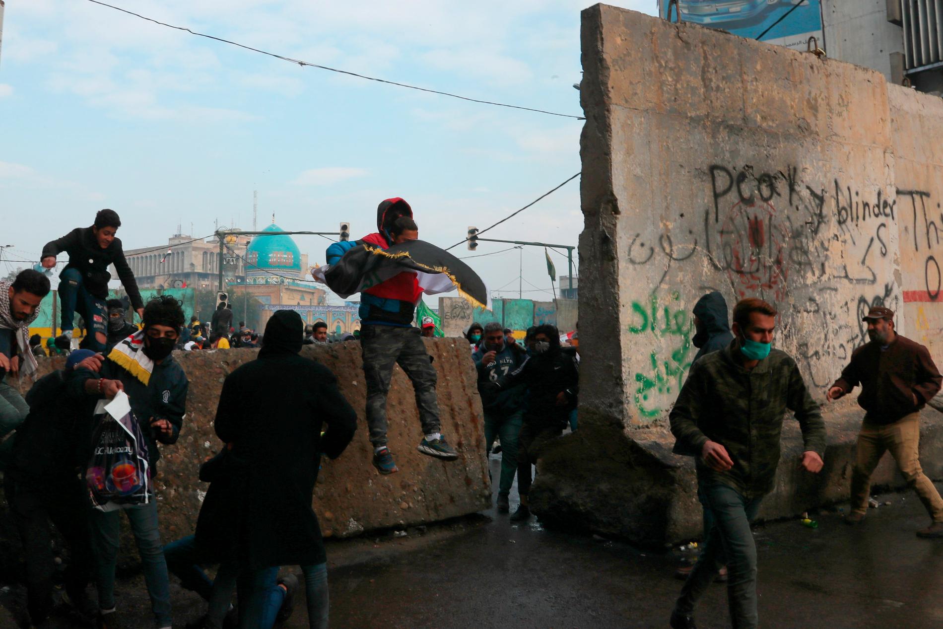 Regeringskritiska demonstranter tar skydd bakom betongavspärrningar i Bagdad under sammandrabbningar med säkerhetsstyrkor.