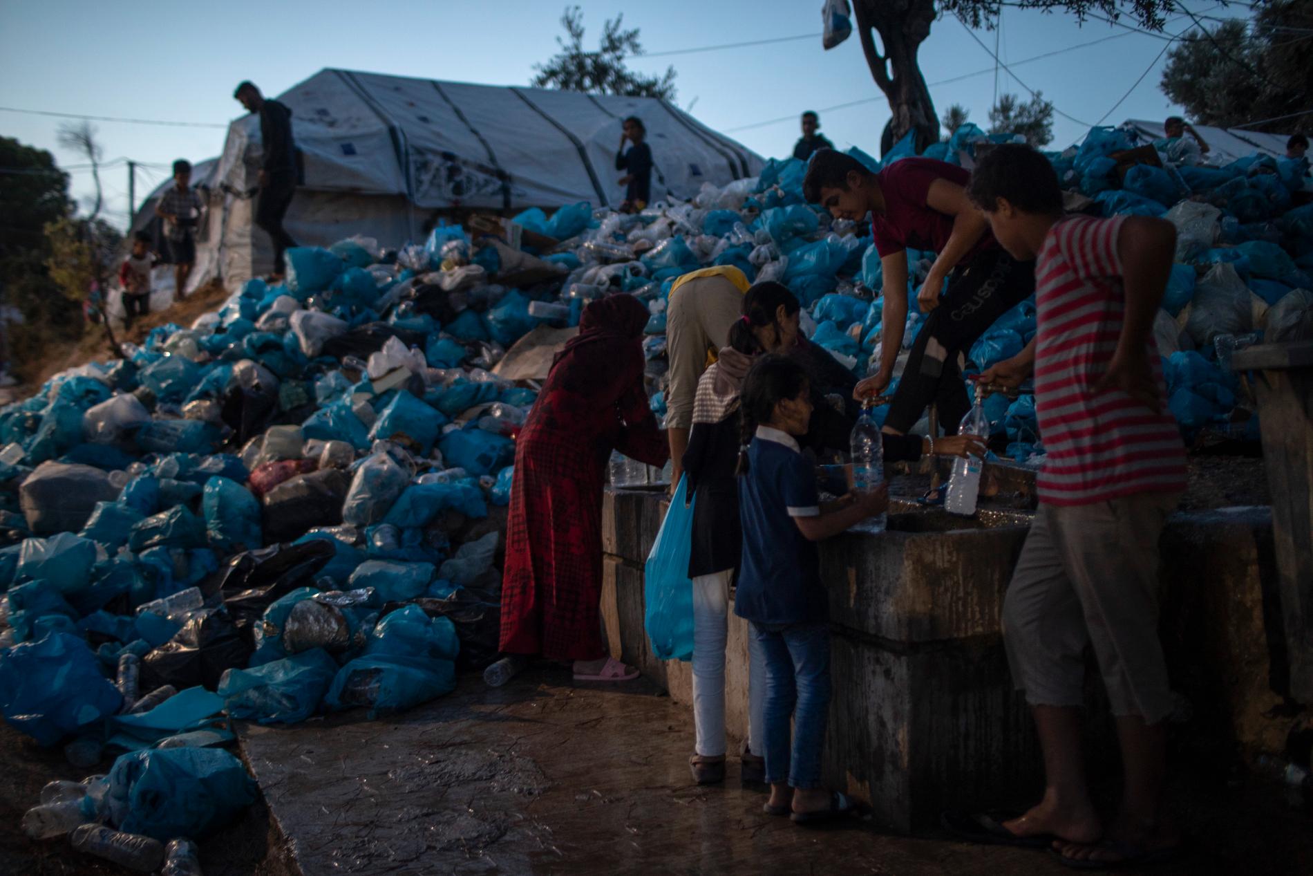 Människor i ett migrantläger på Lebos fyller sina flaskor med vatten bredvid ett berg av sopor. Arkivbild från tidigare i oktober.