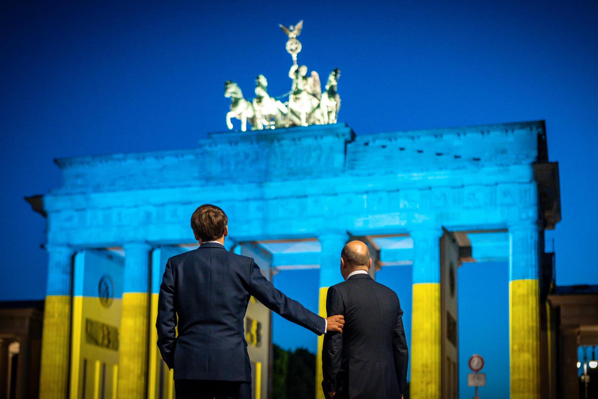 Frankrikes president Emmanuel Macron och Tysklands förbundskansler Olaf Scholz vid Brandenburger Tor, upplyst i ukrainska färger, efter ett möte i Berlin i maj. Arkivbild.