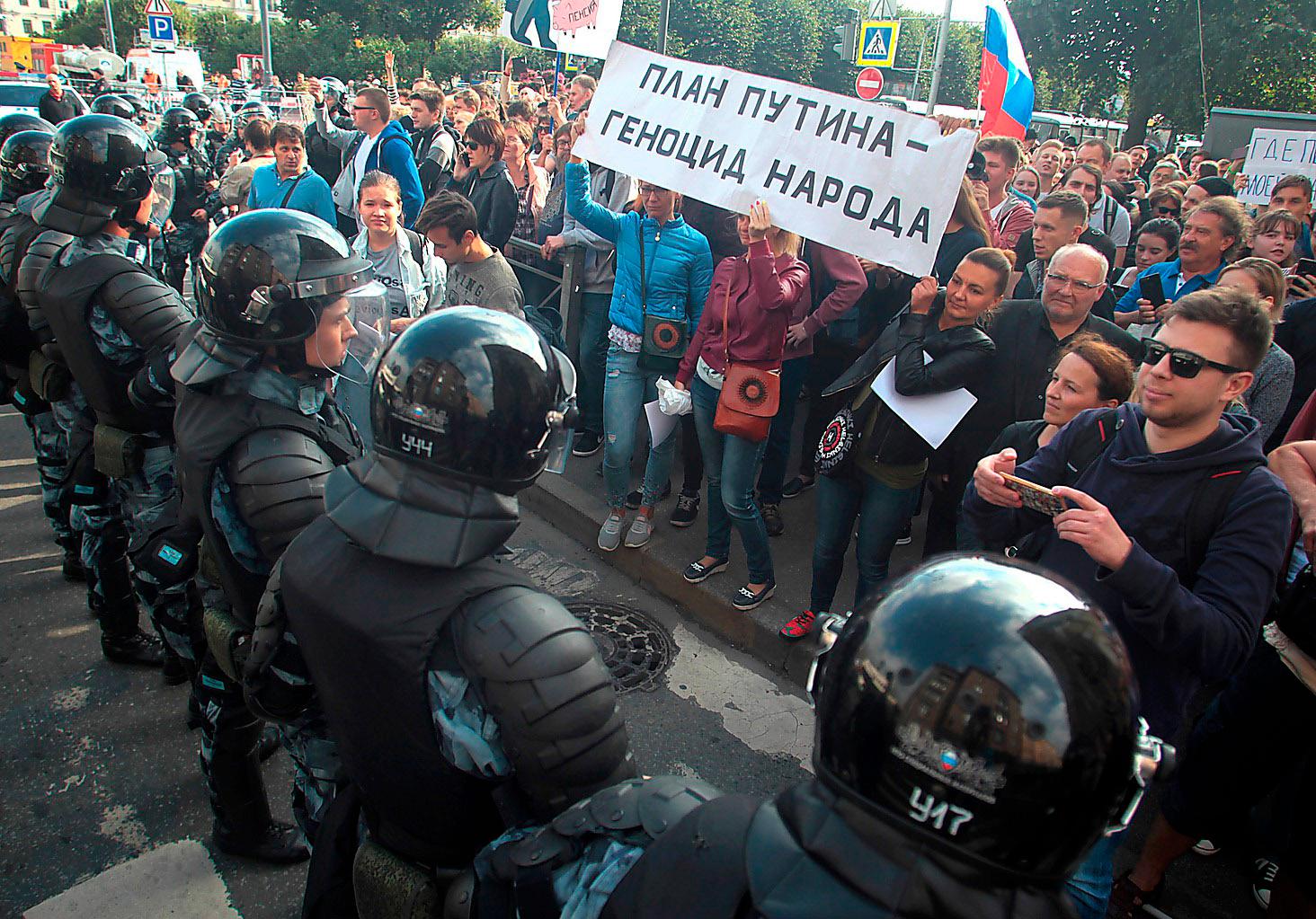 Rysk kravallpolis stoppar demonstranter med banderollen ”Putins plan är folkmord” i samband med demonstrationer mot den nya pensionsreformen  i Sankt Petersburg den 9 september.