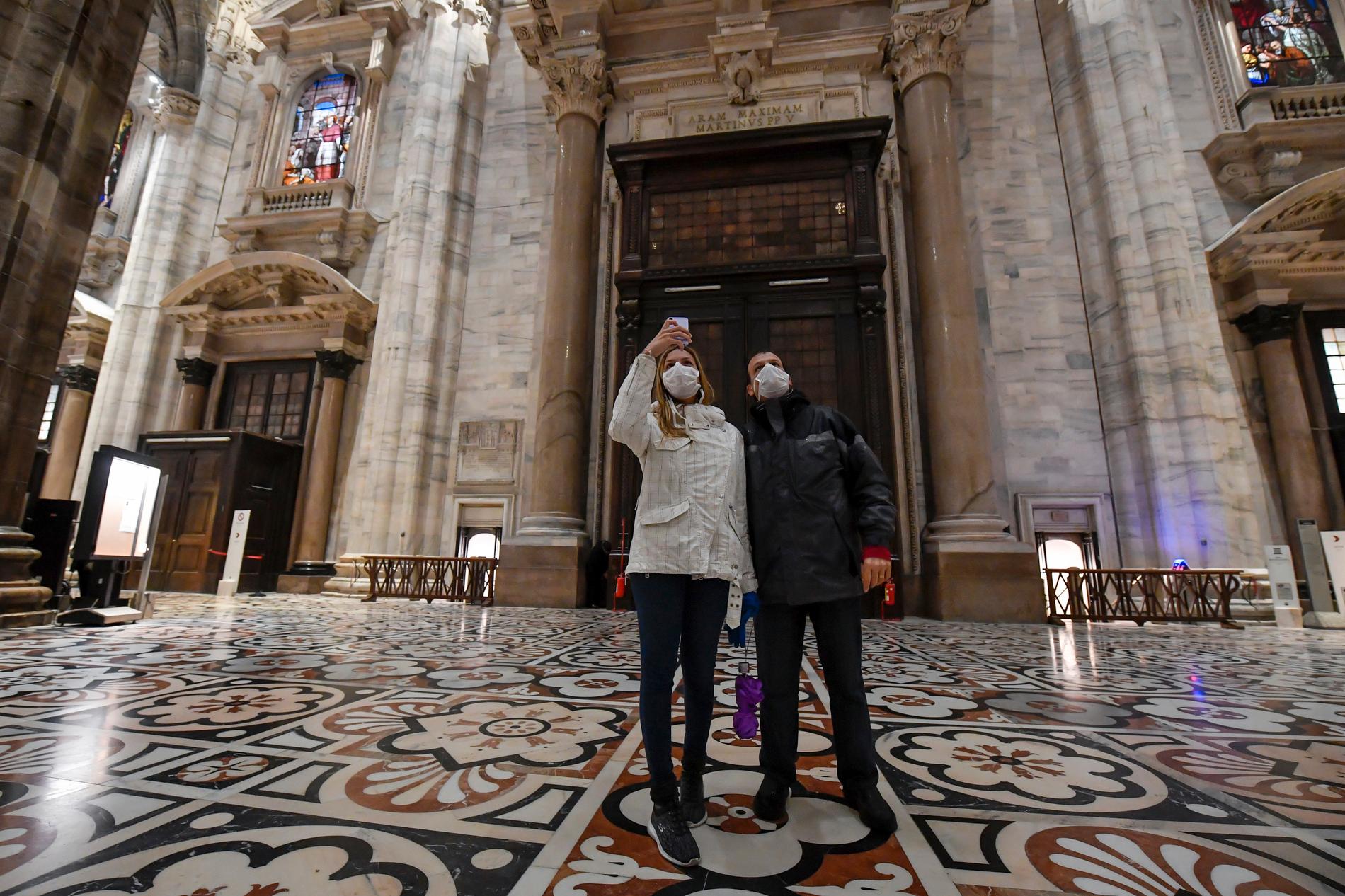 Turister i Milanos katedral Duomo di Milano tar bilder iklädda ansiktsmasker. Milano ligger i Lombardiet, en av de regioner där besökare uppmanas vara uppmärksamma. Arkivbild.