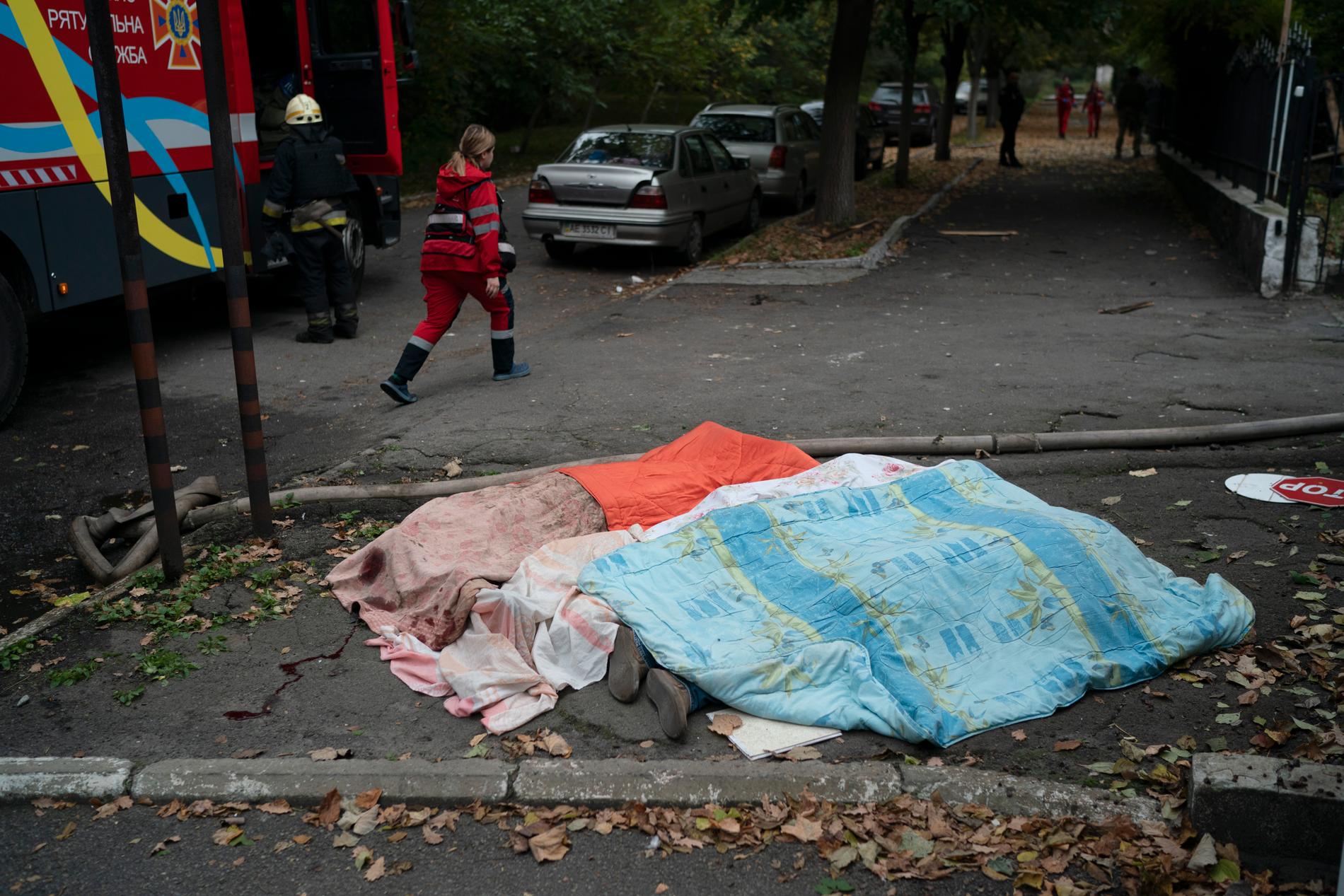 Räddningspersonal passerar tre döda kroppar som täckts med filtar i staden Dnipro, Ukrainas fjärde största stad.
