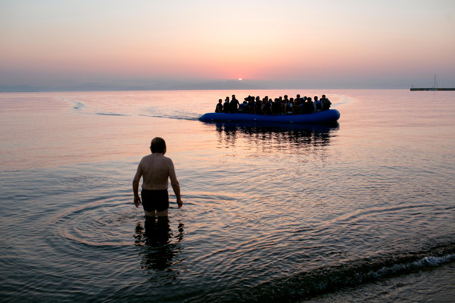 En man tar ett morgonbad på stranden i centrala Kos när en båt med flyktingar anländer. 7 juli 2015.