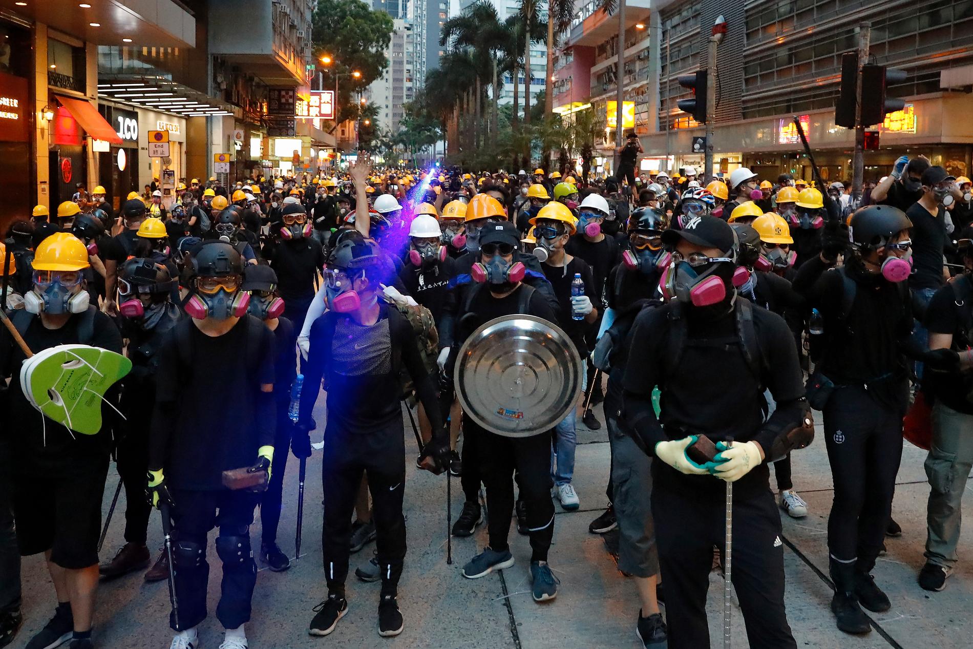 Aktivister i hjälmar och andningsskydd mot tårgasröken konfronterar polisen på en gata i Hongkong under söndagens protester.