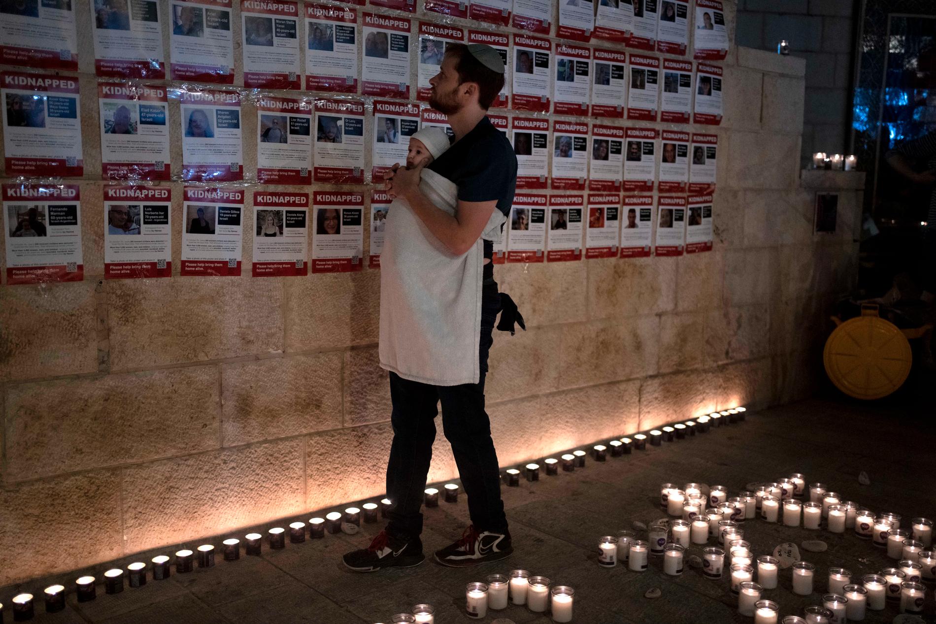 En man med sitt barn tittar på listor över kidnappade israeler på en vägg i Jerusalem.