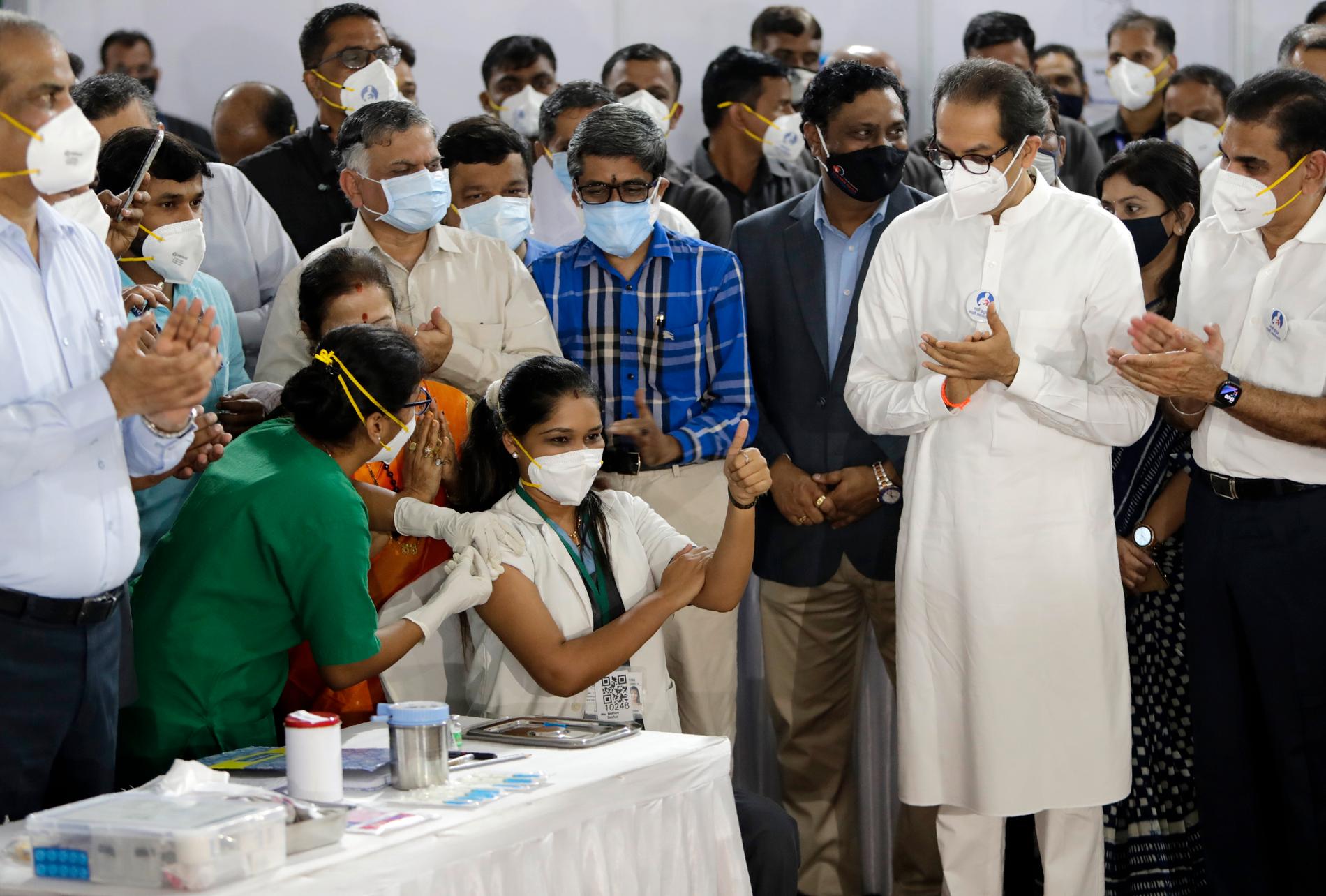 Sjukvårdaren Madhura Patil får sin vaccinspruta i Bombay under lördagen. Delstaten Maharashtras högste minister, Uddhav Thackeray, (till höger i vitt), deltog för att uppmärksamma att Indien nu börjar vaccinera sina medborgare i stor skala.