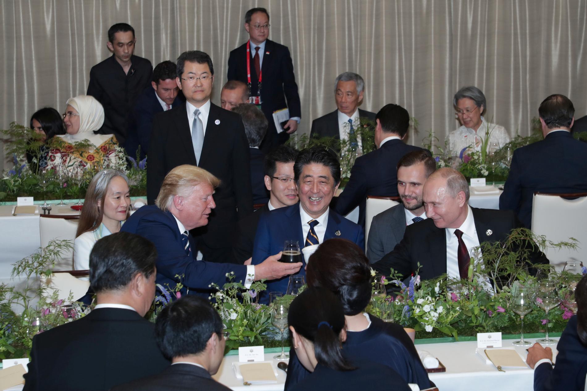 Det vinglas USA:s president Donald Trump håller i möter den vita termosmugg som Rysslands president Vladimir Putin håller fram, och som skymtar framför Japans premiärminister Shinzo Abes slips.