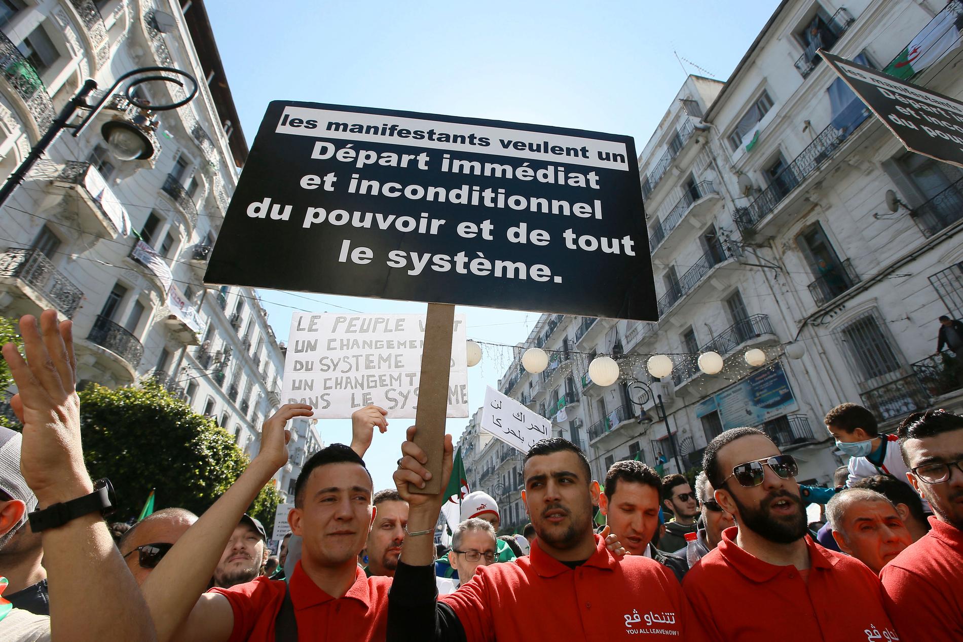 En demonstrant håller upp ett plakat som kräver systemskifte i Algeriet.
