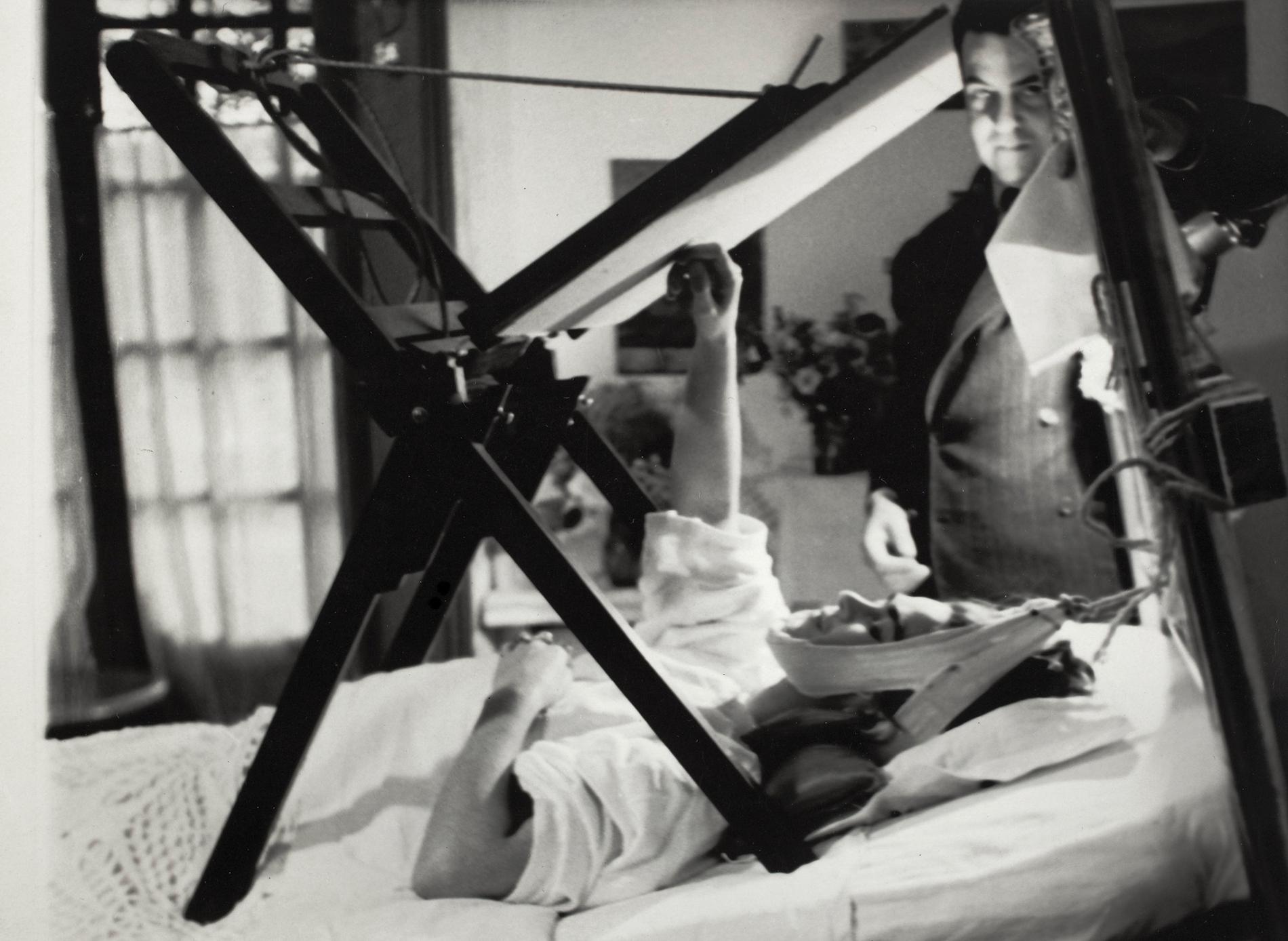 Frida målar i sängen med Miguel Covarrubias stående vid hennes sida, 1940. Pressbild.