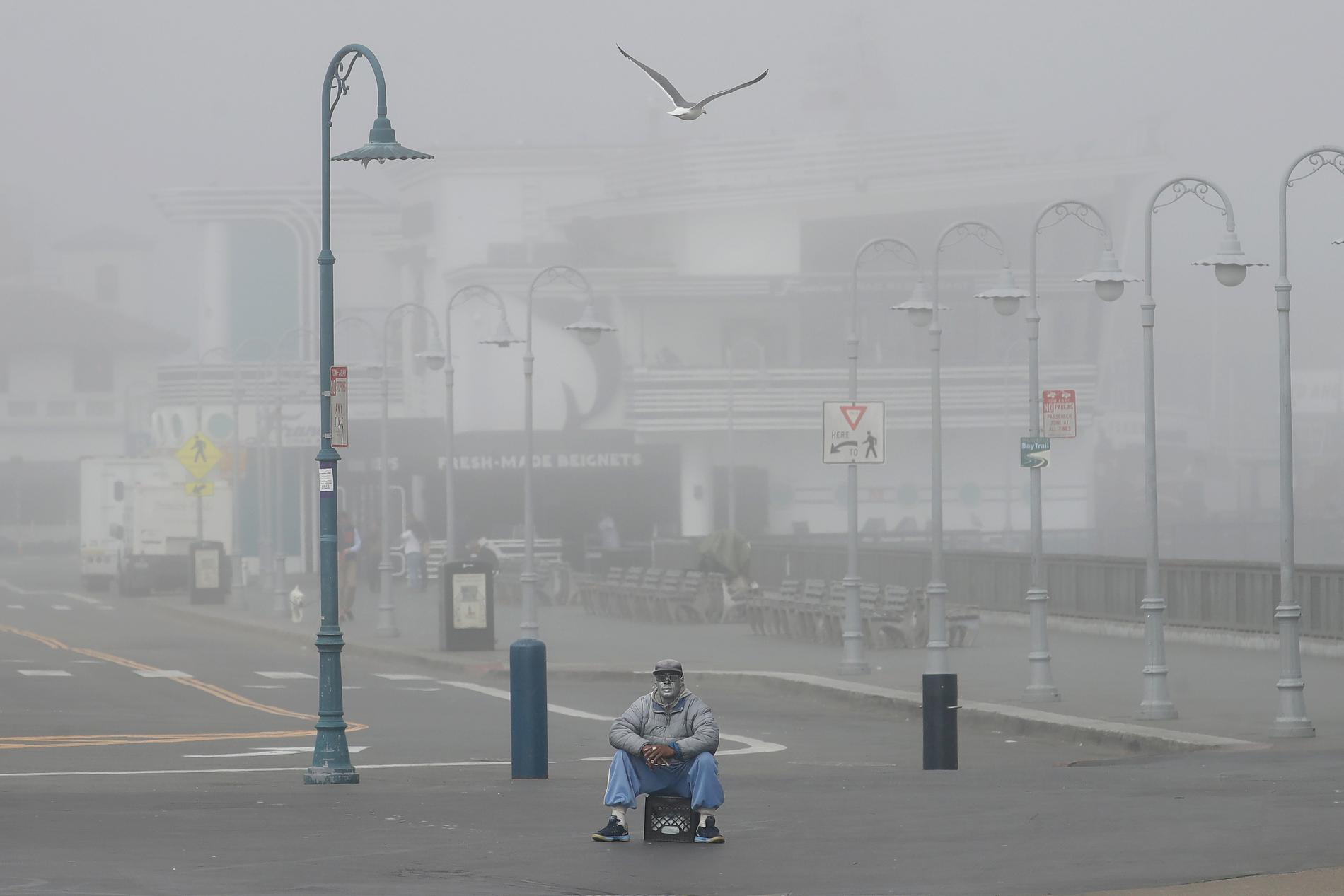En gatuartist sitter ensam i Fisherman's Wharf i San Francisco på torsdagen. Även Kaliforniens invånare beordras att stanna hemma.