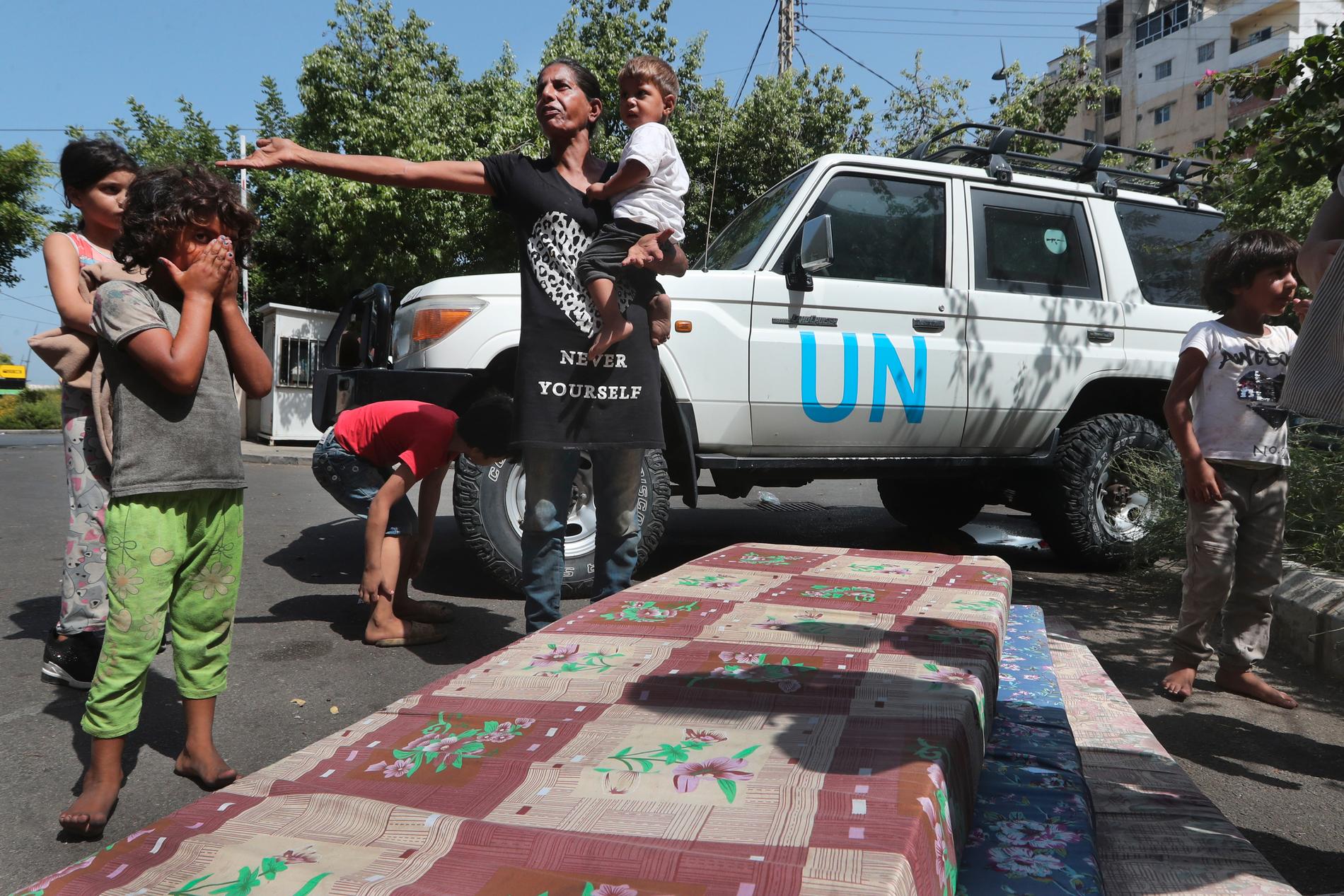 En palestinsk kvinna står med sin familj efter att ha flytt från det palestinska flyktinglägret och väntar att bli flyttade med hjälp av Unrwa (FN:s hjälporganisation för palestinska flyktinga).