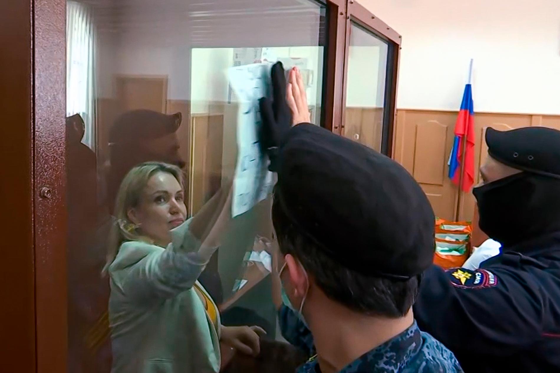 Marina Ovsjannikova håller upp en skylt där det står ”Låt de mördade barnen komma till dig i dina drömmar” – ord som poliserna försöker dölja med sina händer. Bild från augusti 2022. 