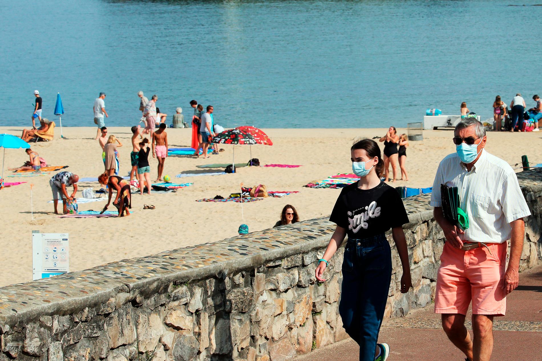 Människor iförda munskydd strosar längs stranden i Saint Jean de Luz, Frankrike. 