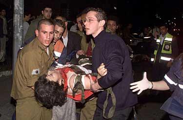 Räddningspersonal hjälper en skadad kvinna till sjukhus. De två bomberna skakade vid halvsjutiden ett område nära gamla busstationen i Tel Aviv.