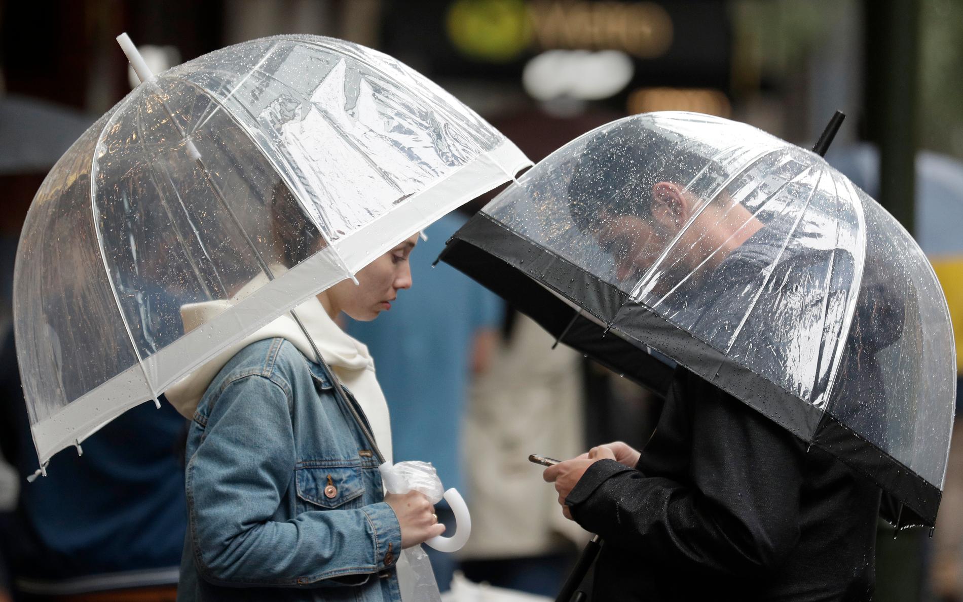 Ett par tar skydd under paraplyer från regnet över Sydney på fredagen.