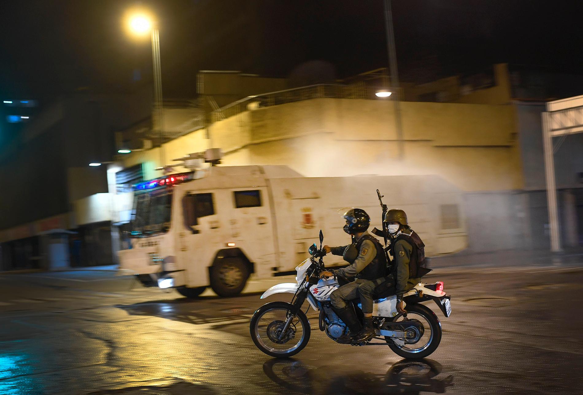 CARACAS, VENEZUELA Beväpnad militär från nationalgardet patrullerar samtidigt som en vattenkanon sprutar desinfektionsmedel i Caracas på lördagen.