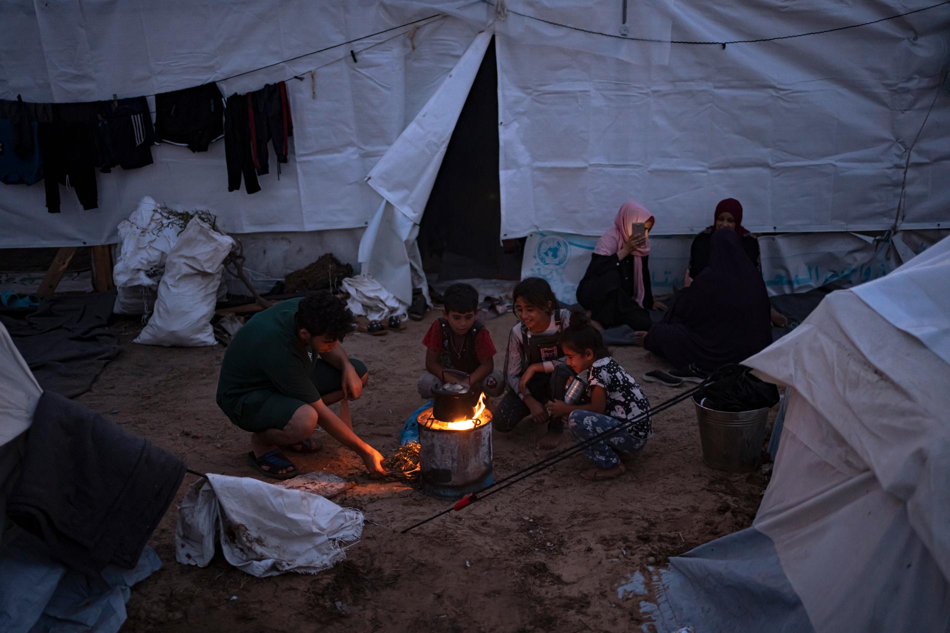 Palestinier som flytt från Israels bombningar sitter vid en brasa, utanför tält försedda av FN:s utvecklingsprogram (UNDP), i Khan Younis vid Gazaremsan, den 31 oktober, 2023.