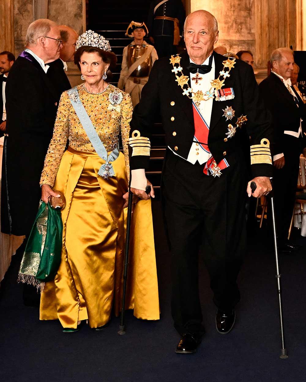 Drottning Silvia i gult siden och med armen på norska kung Harald. 