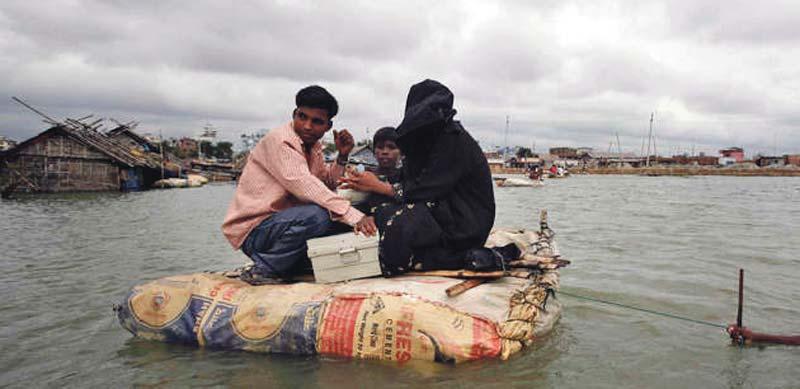 En familj räddar sig undan vattenmassorna på en improviserad flotte vid en översvämning i kåkstaden Kamragir Char i Bangladesh.