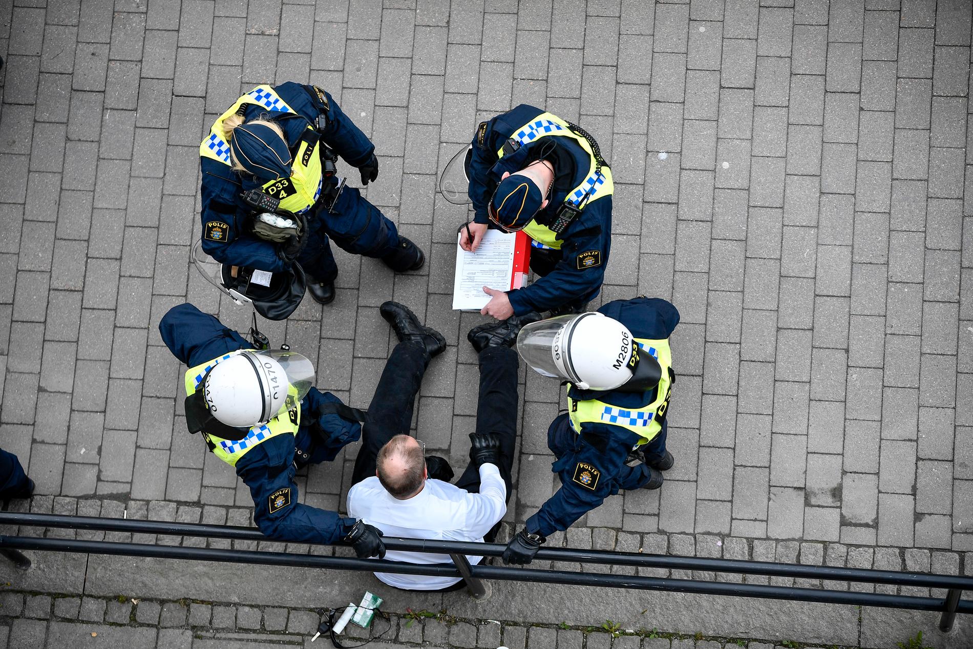En medlem ur nazistiska organisationen Nordiska motståndsrörelsen (NMR) sitter på backen omringad av poliser. Arkivbild.