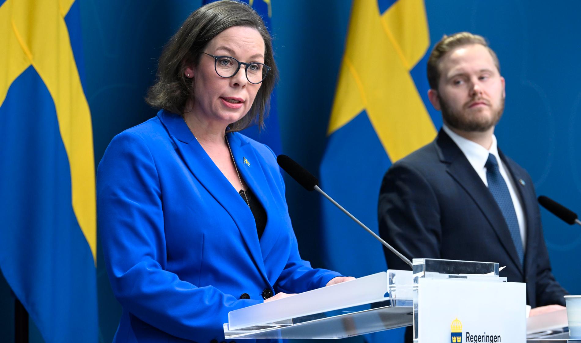 Sverigedemokraternas Henrik Vinge tittar över axeln på migrationsminister Maria Malmer Stenergard (M).