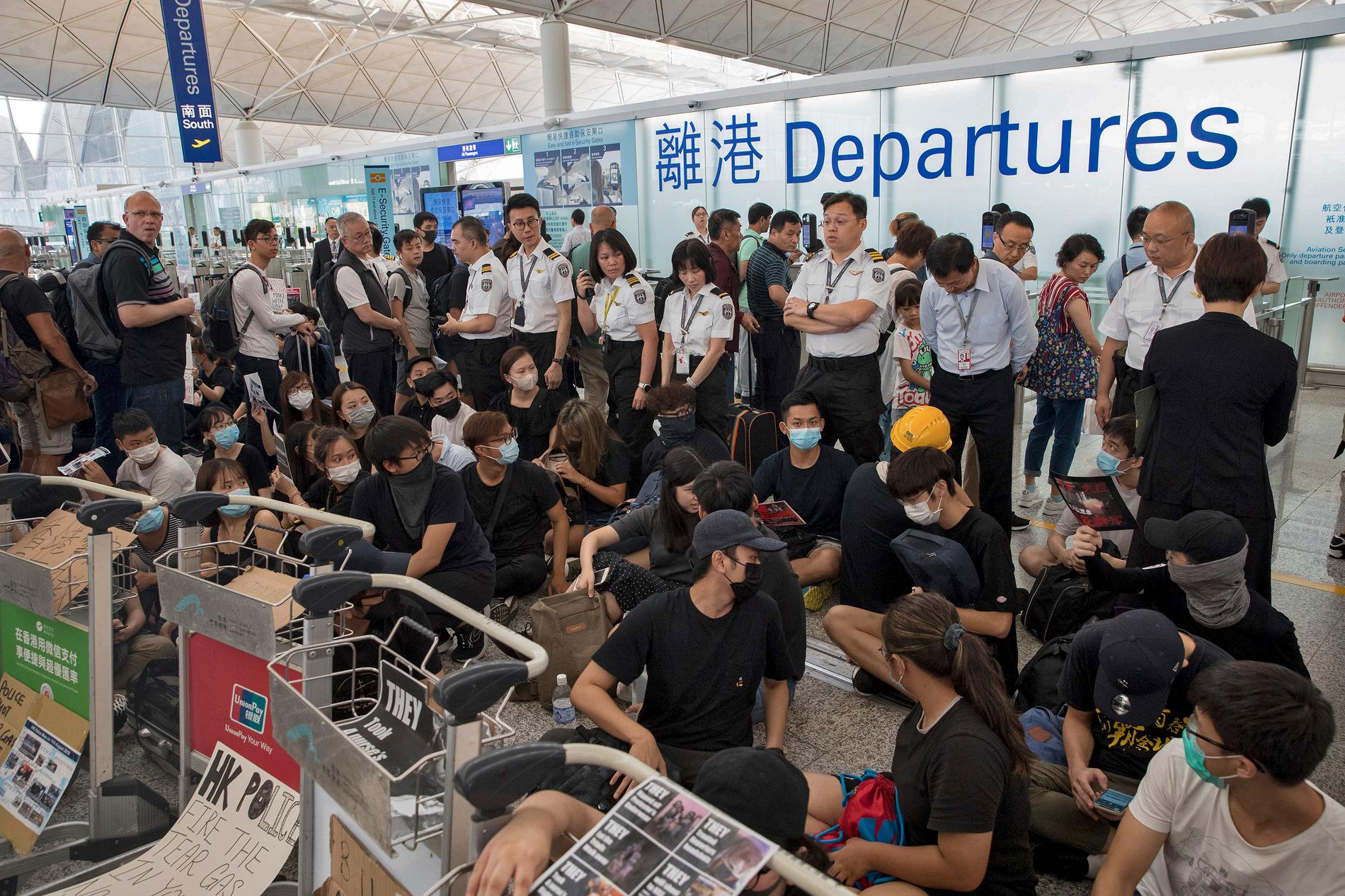 Flygplatspersonal vaktar bakom demonstranter vid avgångshallen på Hongkongs internationella flygplats.