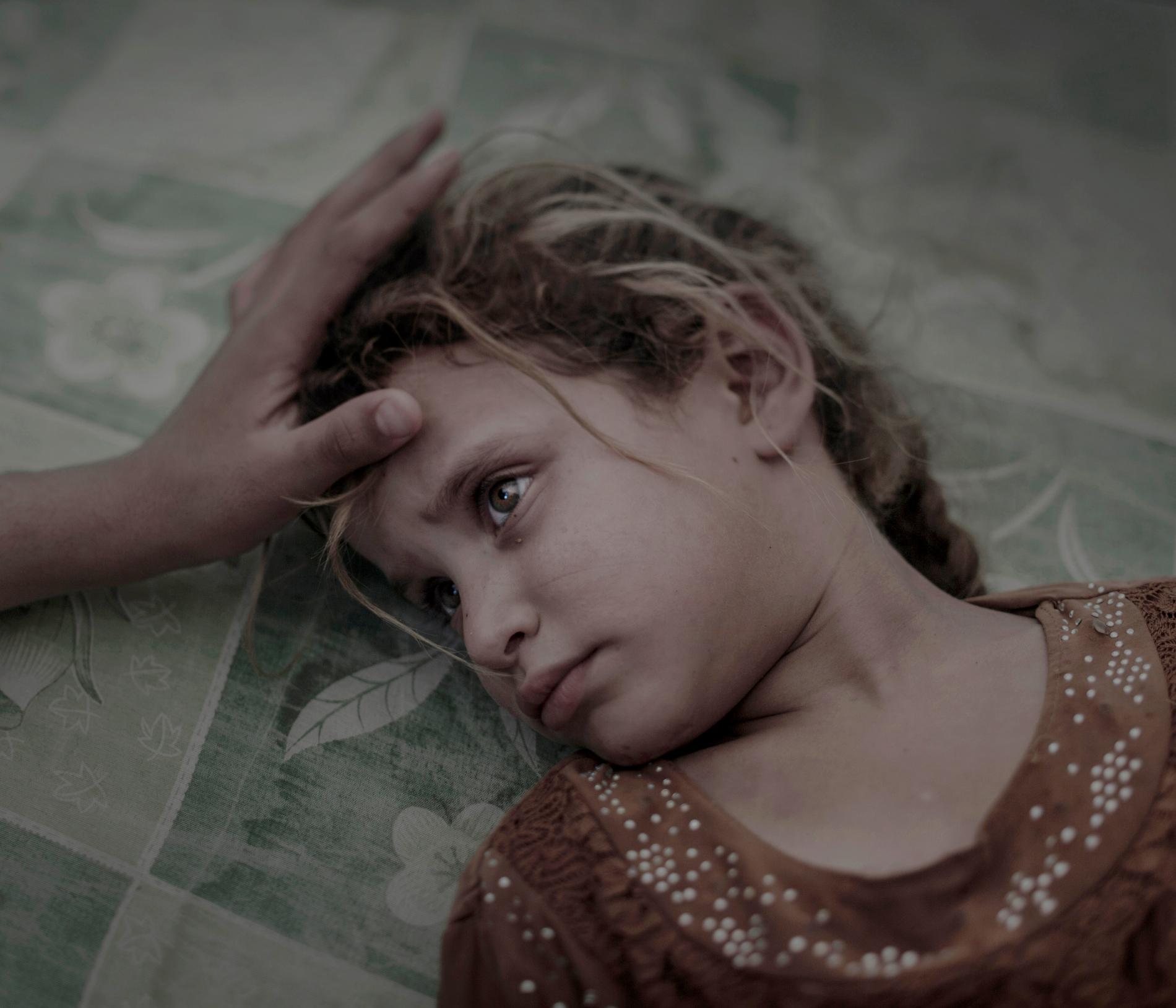 Porträtt Förstapris. Maha och hennes familj flydde från byn Hawiga utanför Mosul. Skräcken för IS och bristen på mat gjorde att de var tvungna att lämna sitt hem, berättar hennes mamma. Nu ligger Maha på en smutsig madrass i det överfulla transit-tältet i flyktinglägret Debaga. ”Jag drömmer inte och jag är inte rädd för någonting längre”, säger Maha tyst, samtidigt som hennes mammas hand stryker henne över håret. 