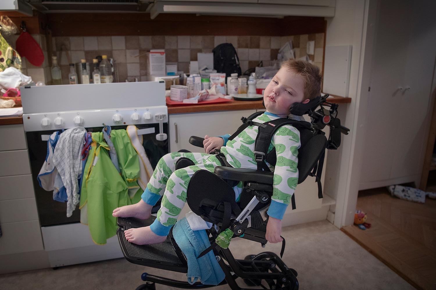 Olof sitter fastpänd med stöd för nacken i sin  rullstol. Mycket av skötseln av Olof är medicinsk vård dygnet runt. "Inget av det vi gör liknar normalt föräldraansvar", säger Karolina Hermansson.